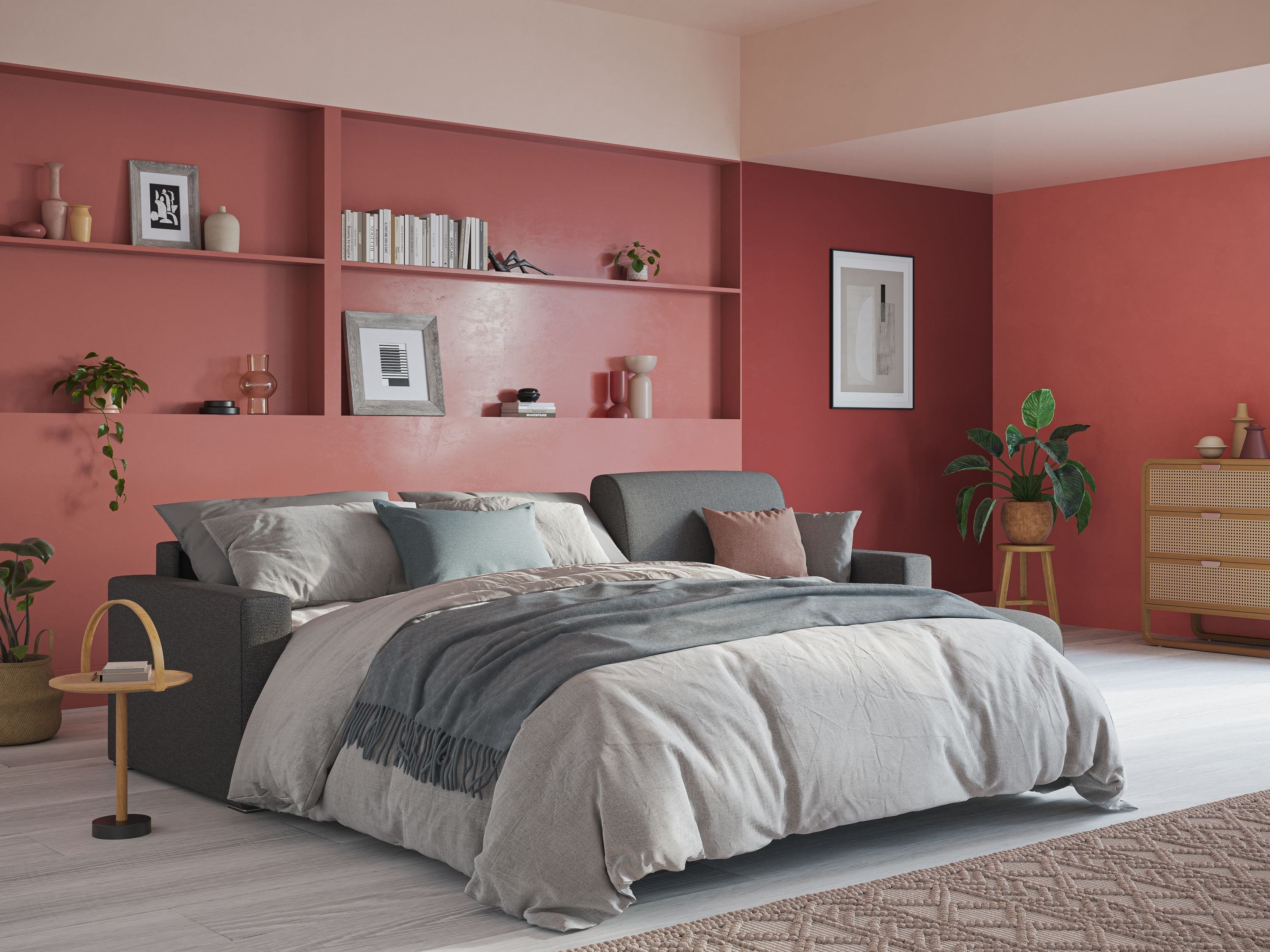 Una camera da letto moderna con un letto grigio, biancheria da letto blu e tortora, pareti con accenti rossi e rosa, scaffali con libri e decorazioni, piante in vaso e una cassettiera in vimini nell'angolo su un pavimento in legno chiaro.