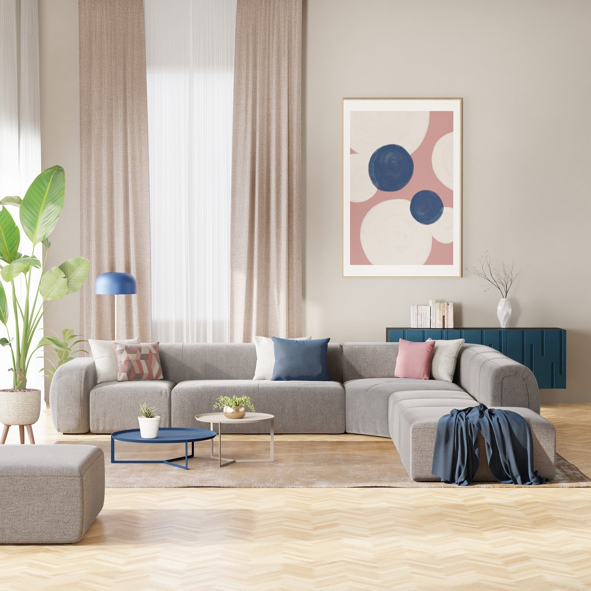 Divani angolari componibili grigio per un soggiorno moderno con un tavolino rotondo, con un vaso, un tavolino laterale con fiori, un quadro incorniciato su una parete blu, lampade a sospensione, una grande finestra e tende beige.