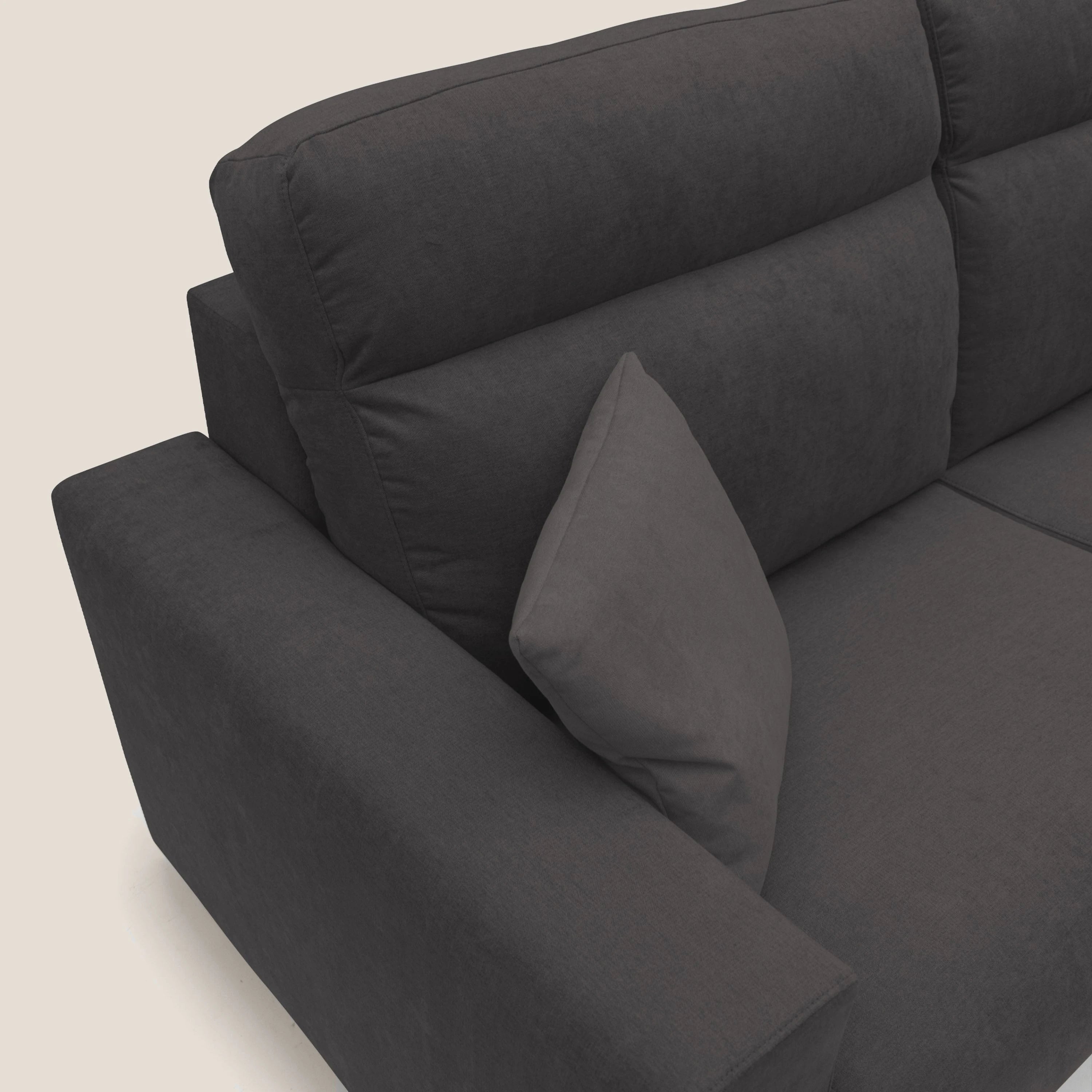 Primo piano del lato sinistro di un divano imbottito grigio scuro con bracciolo arrotondato e seduta imbottita, su uno sfondo chiaro e semplice. Sono visibili solo parte dello schienale e della seduta.