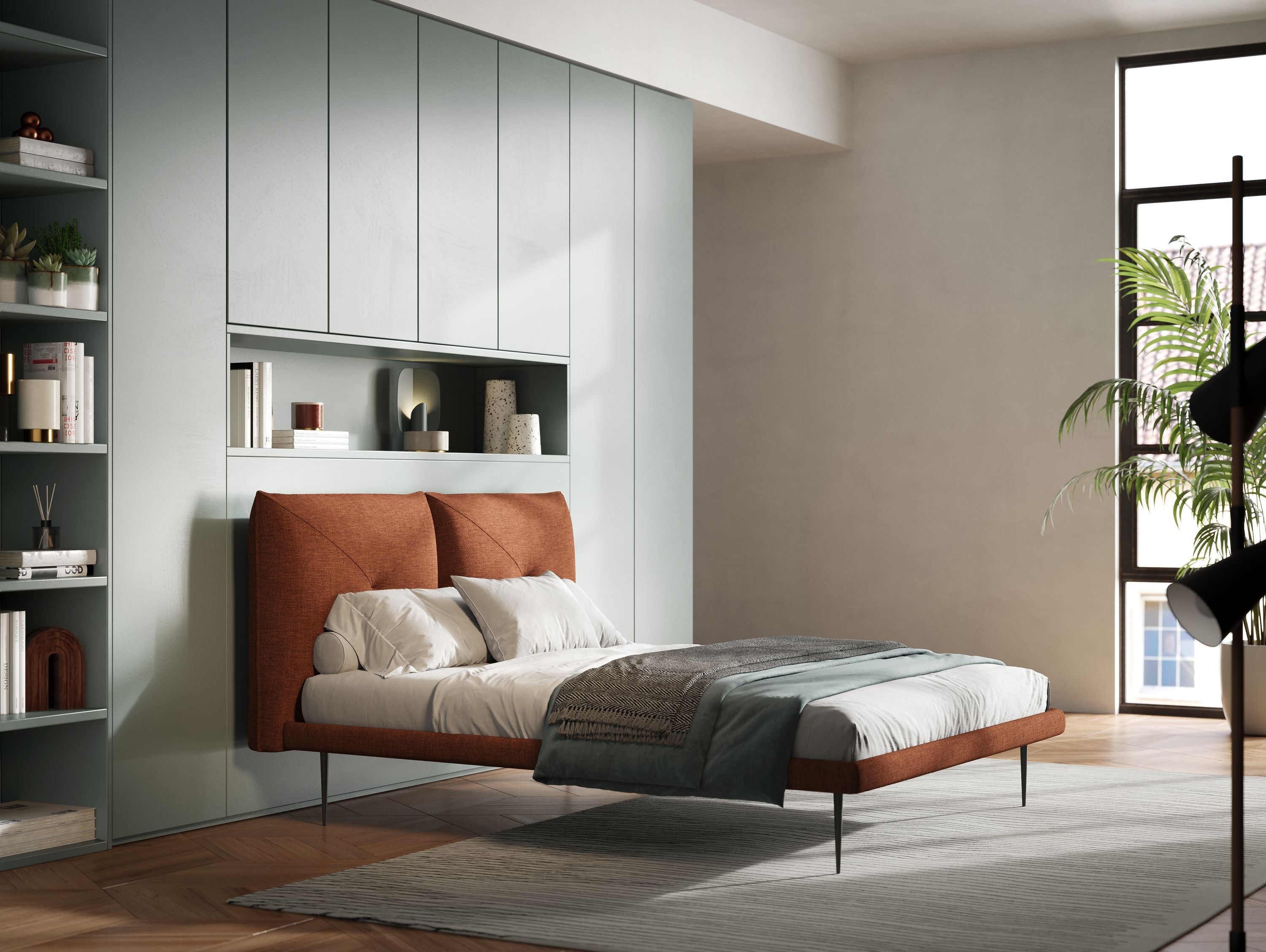 Una camera da letto moderna con un letto color ruggine, biancheria da letto bianca e grigia, armadi color salvia a muro, scaffali decorati, una grande finestra che lascia entrare la luce del sole e un tappeto chiaro sul pavimento in legno.