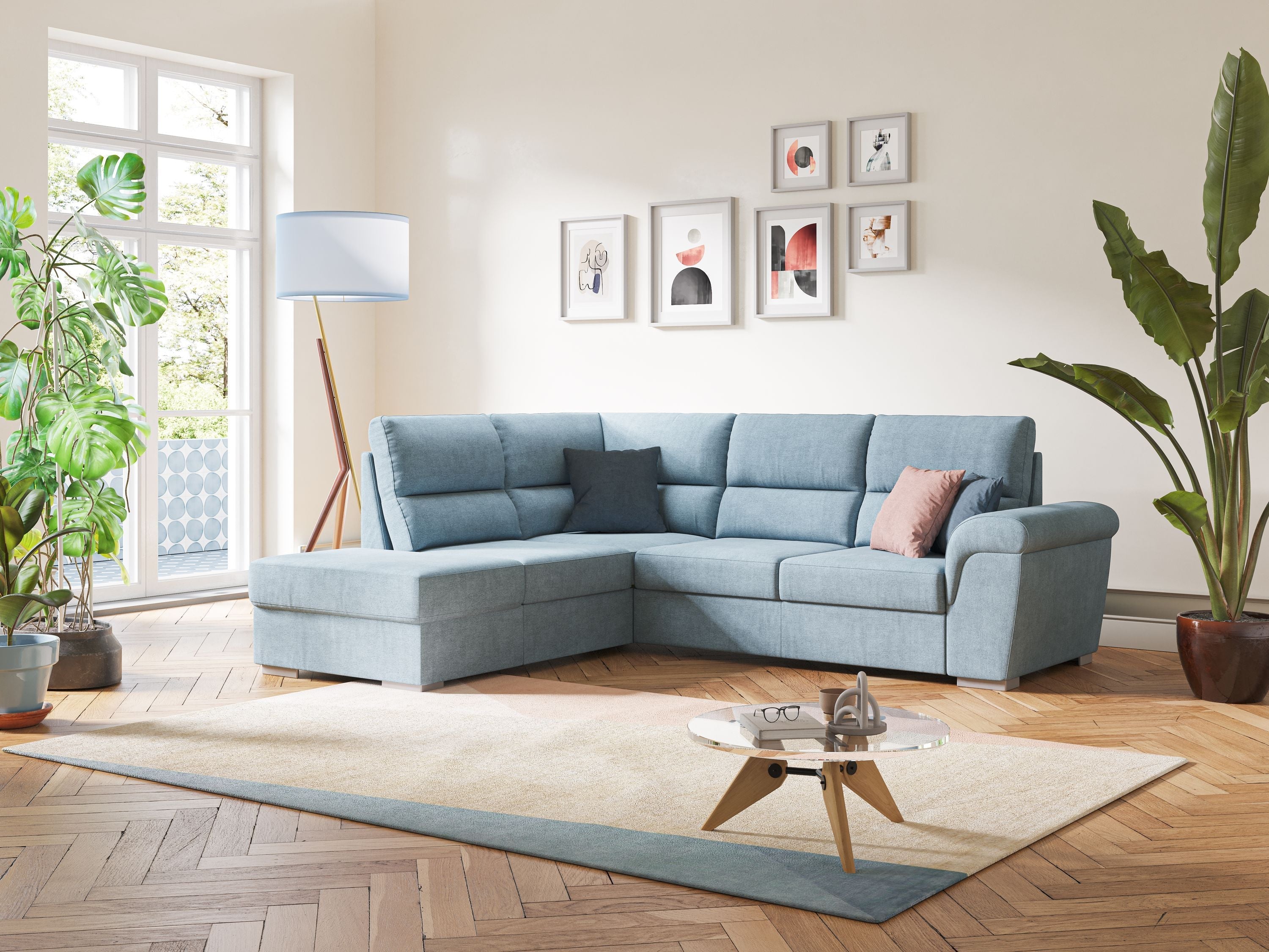 Un soggiorno moderno con un divano componibile azzurro, un tappeto beige, un tavolino rotondo, grandi piante verdi, quadri incorniciati e un'alta lampada da terra vicino a una finestra da cui entra a fiotti la luce del sole.