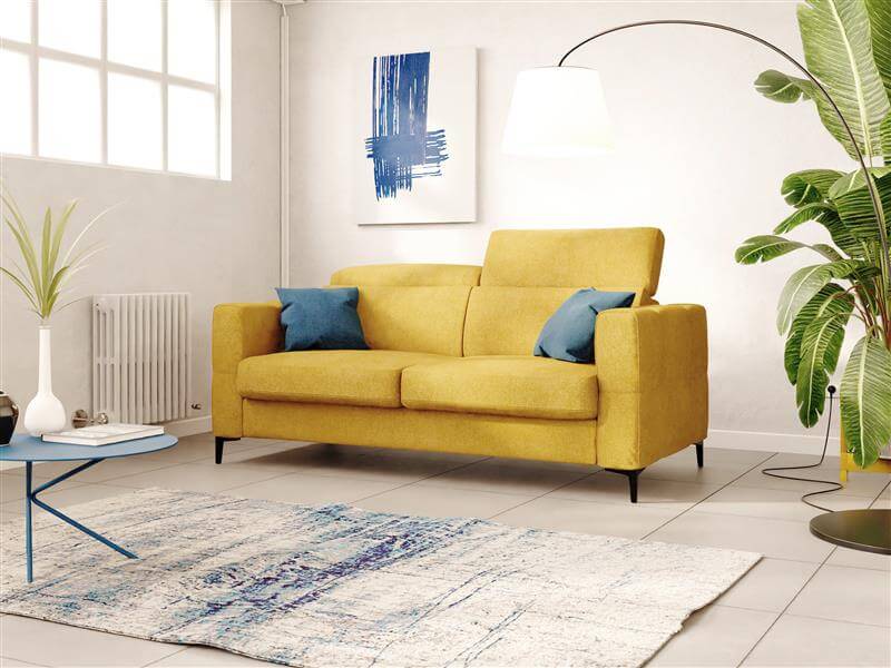 Un soggiorno moderno con un divano giallo, cuscini blu e gialli, quadri astratti alle pareti, una lampada da terra alta, una pianta verde, un tappeto bianco e un tavolino con una pianta in vaso, il tutto su un pavimento piastrellato.