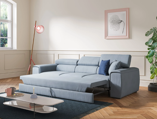 Un soggiorno moderno è caratterizzato da un divano letto azzurro, un cuscino blu navy, un tavolino da caffè bianco con libri e una tazza, un'alta lampada da terra rosa, una stampa di foglie incorniciata e una grande pianta frondosa.