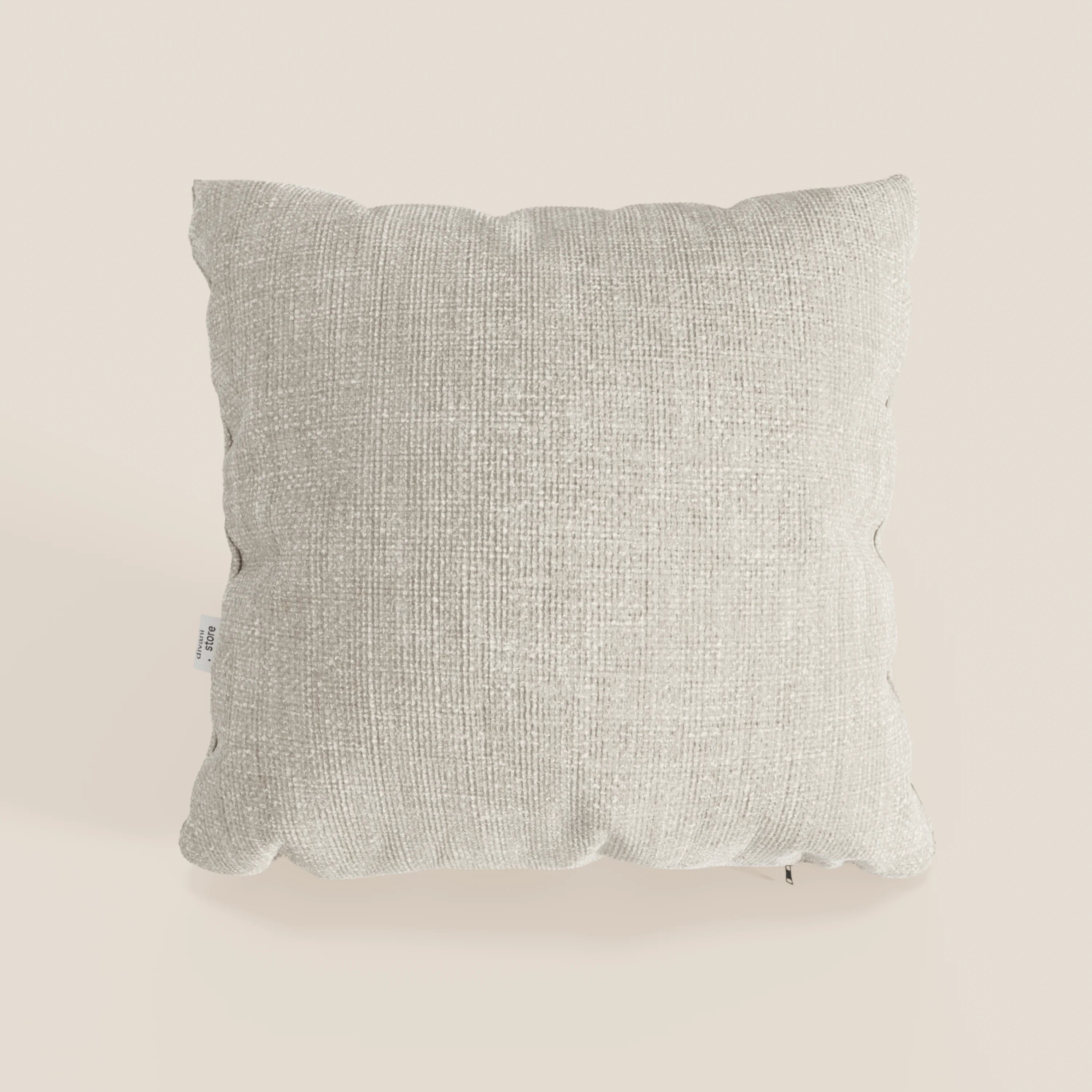 Il cuscino Lyon 45x45 cm di Divani.Store, in morbido tessuto impermeabile T06 panna, si trova su uno sfondo bianco sporco. Presenta un motivo sottile, una piccola etichetta di cucitura bianca e ombre delicate sotto il cuscino decorativo.