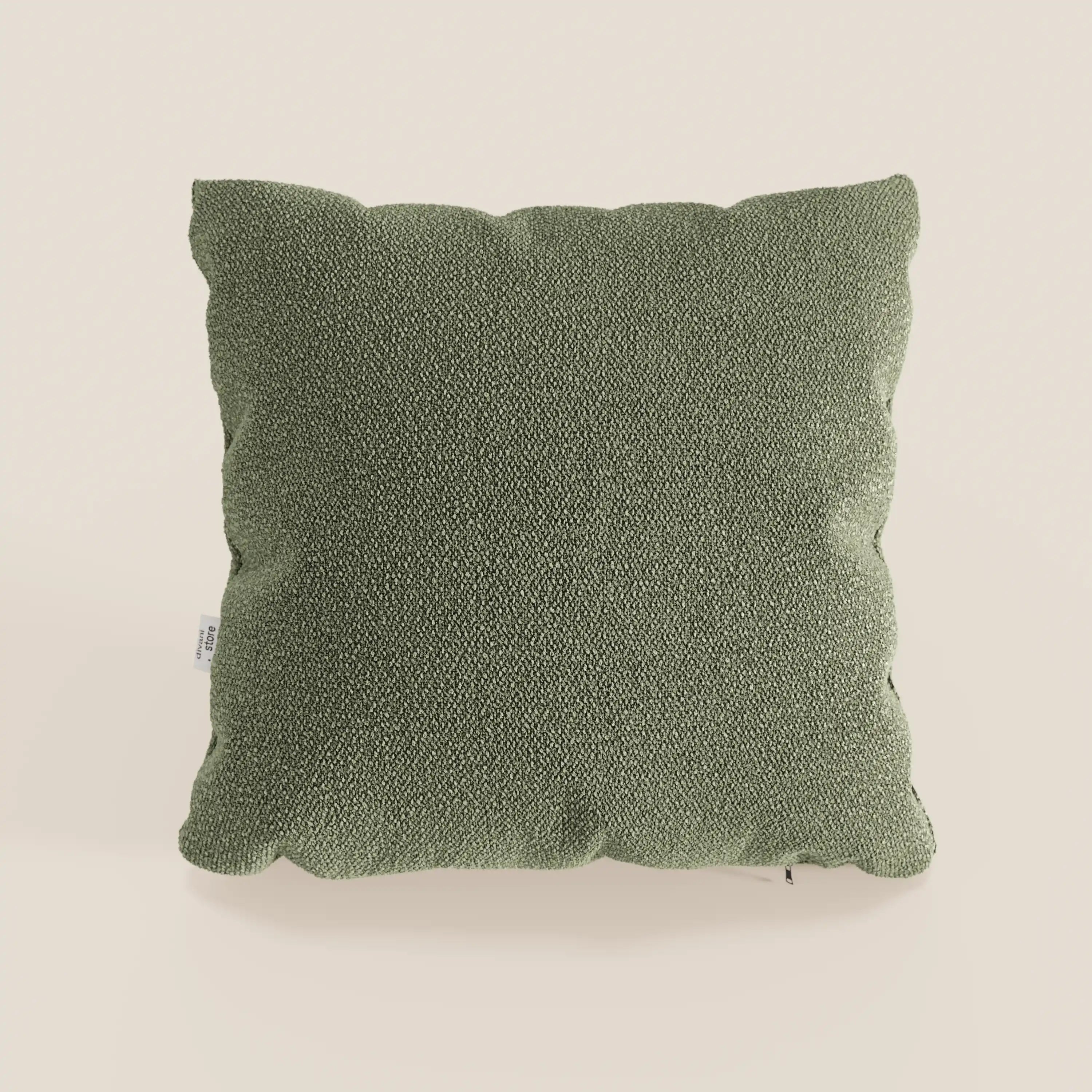 Il cuscino quadrato Lambada verde di Divani.Store poggia su uno sfondo beige chiaro, mostrando il suo sottile motivo intrecciato e gli angoli arrotondati. Realizzato in tessuto smacchiabile e impermeabile T33, fresco e dall'aspetto naturale.