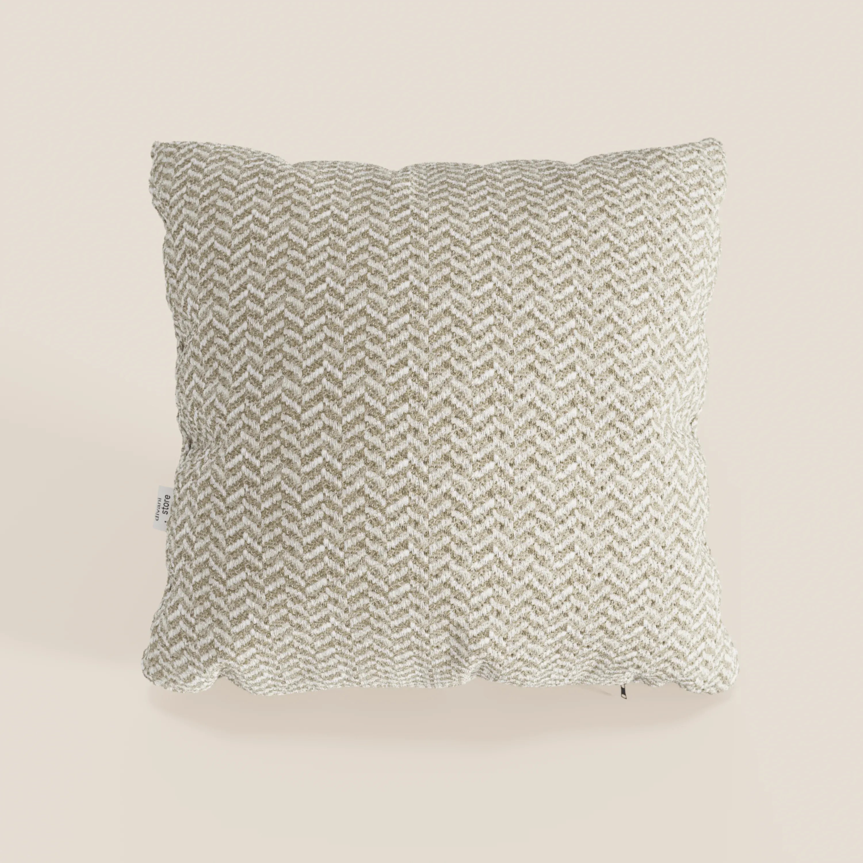Il cuscino Sorrento 45x45 in lino | Eleganza Naturale di Divani.Store, caratterizzato da un motivo a spina di pesce nei toni del beige e dell’avorio, si distingue su uno sfondo neutro chiaro con un’etichetta in tessuto bianca visibile sul bordo sinistro.