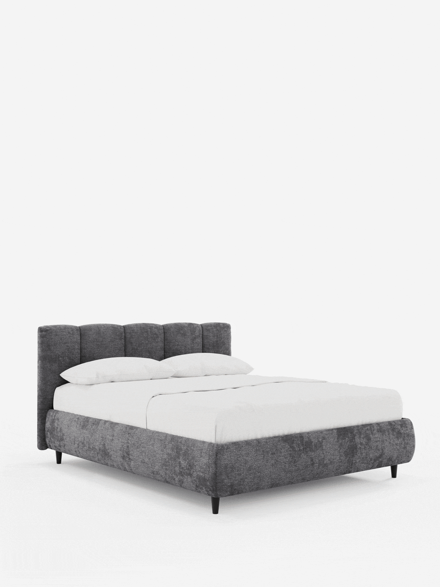ARKAM: letto imbottito con contenitore e testiera a lavorazione verticale, color grigio scuro, con lenzuola bianche, su gambe corte nere affusolate, su sfondo bianco.