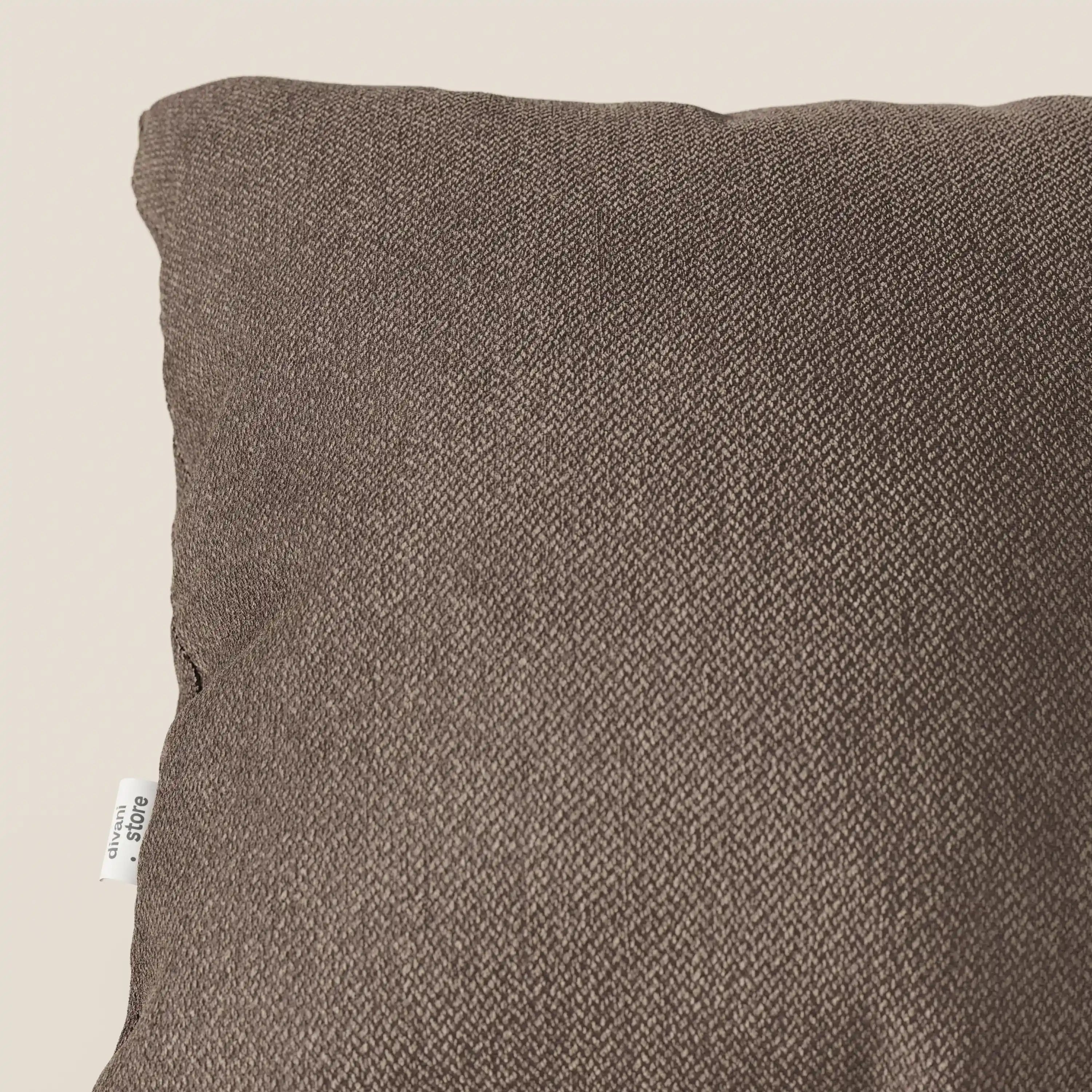 Primo piano di un cuscino Sogno di Divani.Store in morbido tessuto SMACCHIABILE T05 marrone, caratterizzato da un sottile motivo intrecciato e da una piccola etichetta bianca. Solo la parte superiore sinistra è visibile su uno sfondo beige chiaro.
