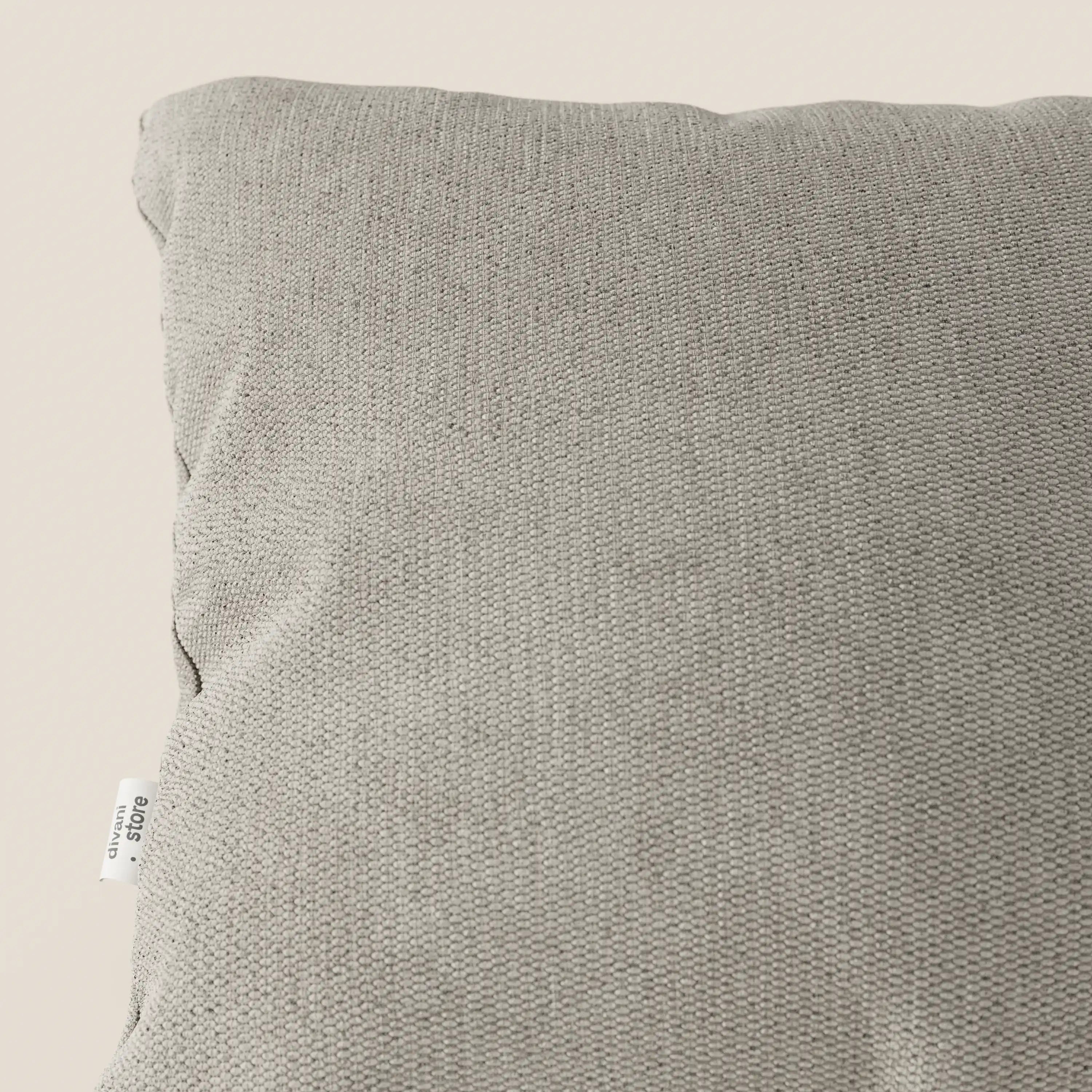 Primo piano dell'angolo superiore sinistro del cuscino Miami 45x45 in morbido tessuto impermeabile T14 tortora di Divani.Store, con una piccola etichetta bianca sulla cucitura. Lo sfondo neutro evidenzia il rivestimento morbido al tatto e lavabile.