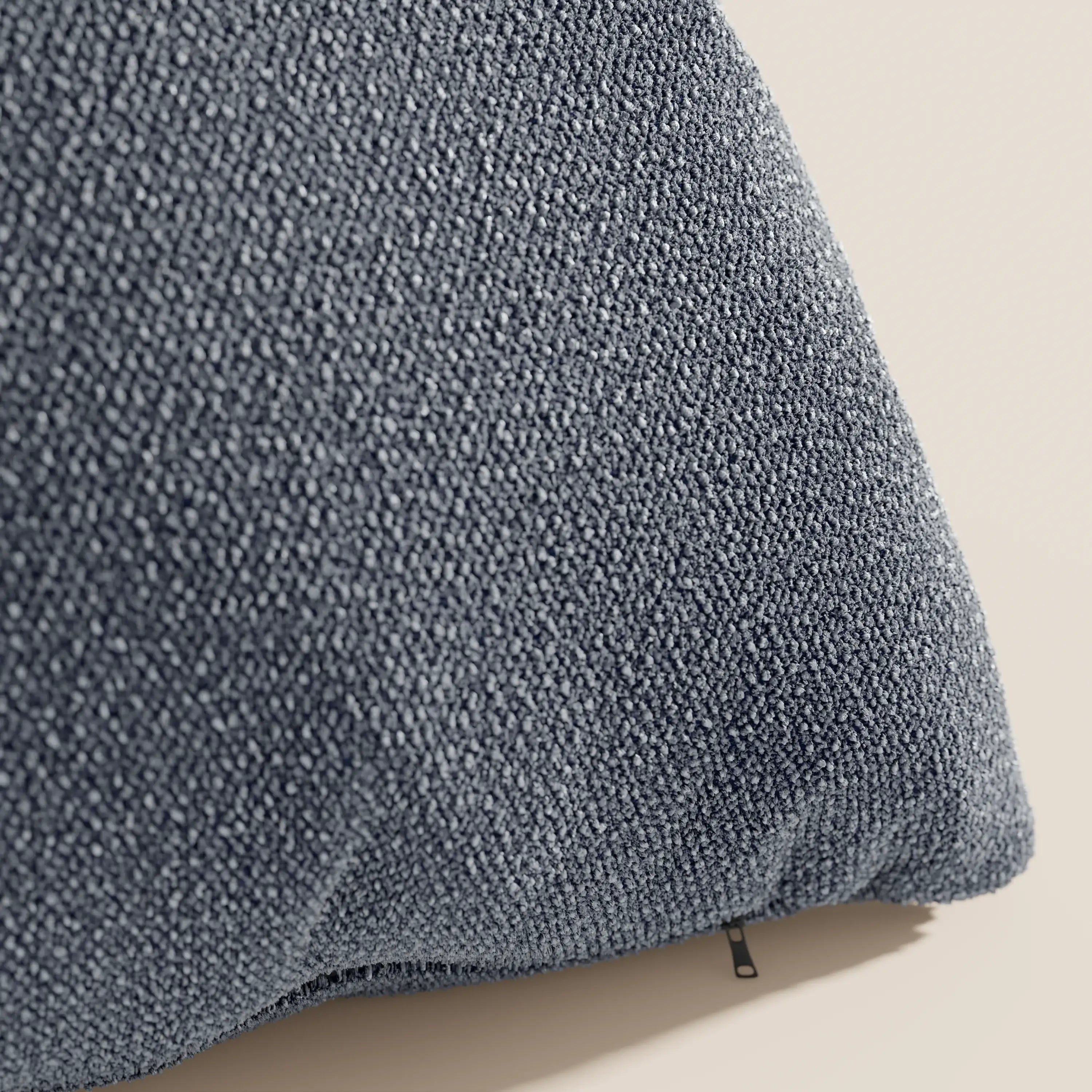 Primo piano del cuscino Lambada di Divani.Store in blu scuro, caratterizzato da una trama a boucle con piccoli passanti e una sottile cerniera nera. Realizzato in tessuto naturale simil-cotone impermeabile e antimacchia.
