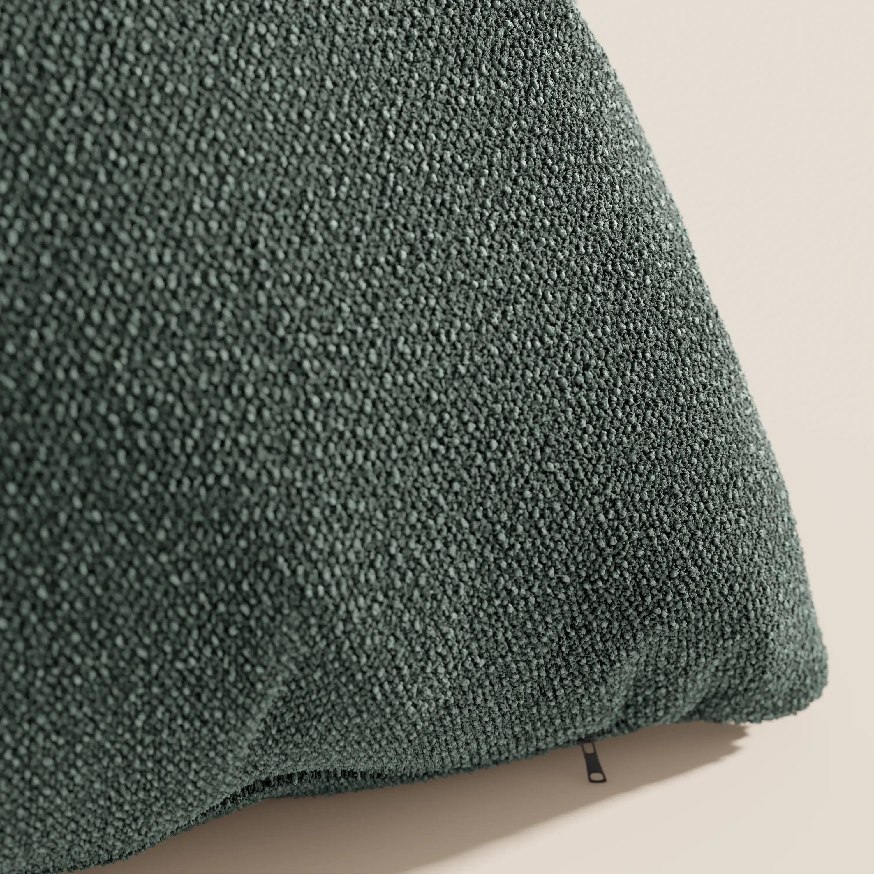 Primo piano del cuscino Lambada di Divani.Store in verde scuro, realizzato con un tessuto di cotone fresco, antimacchia e impermeabile di aspetto naturale (T33), con una trama ad anelli. Il cuscino poggia su uno sfondo beige chiaro, con il tiretto della cerniera visibile in basso.