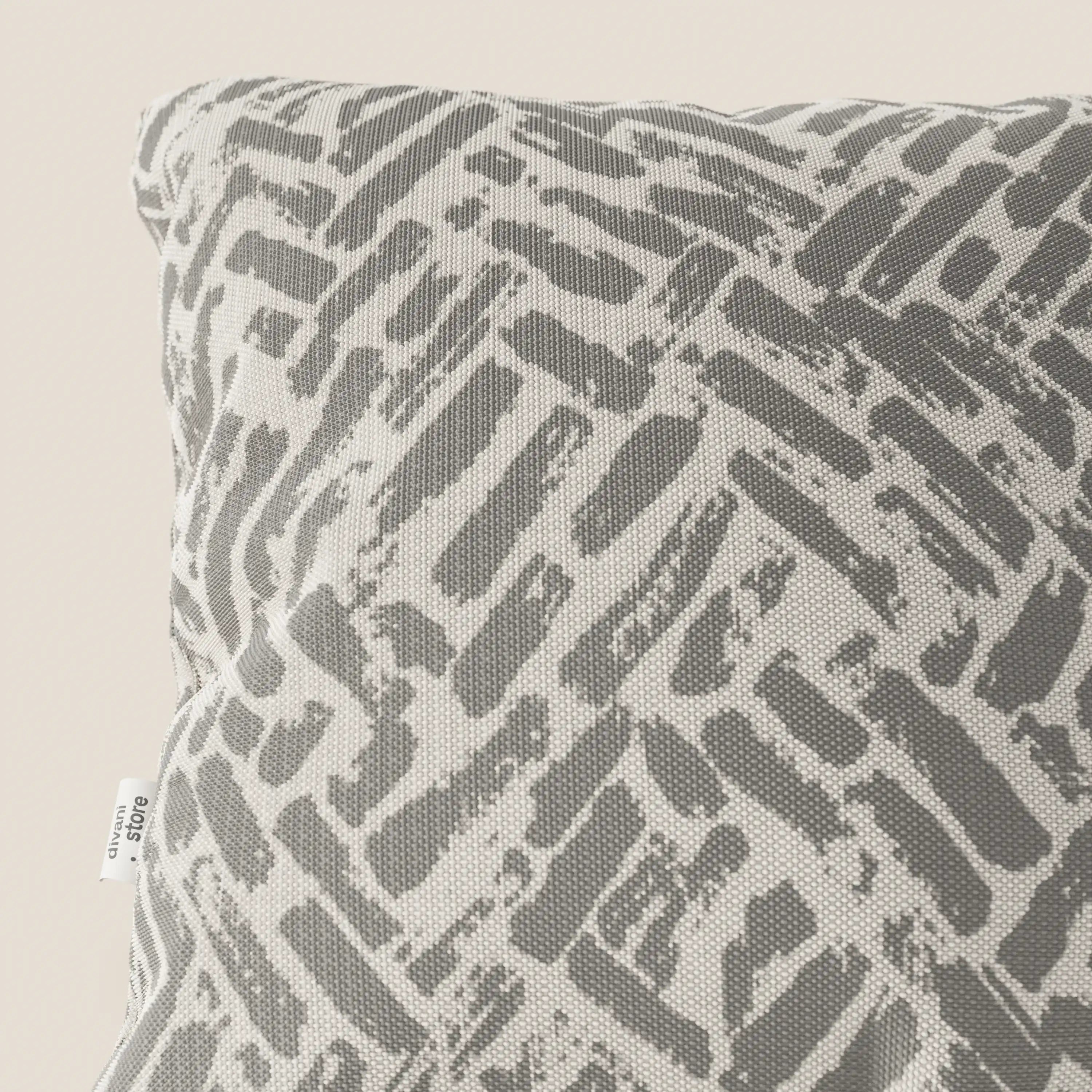 Primo piano del cuscino geometrico Brick di Divani.Store, in tessuto grigio idrorepellente. Il cuscino presenta un motivo astratto e strutturato con una targhetta bianca sul lato, su uno sfondo beige chiaro.