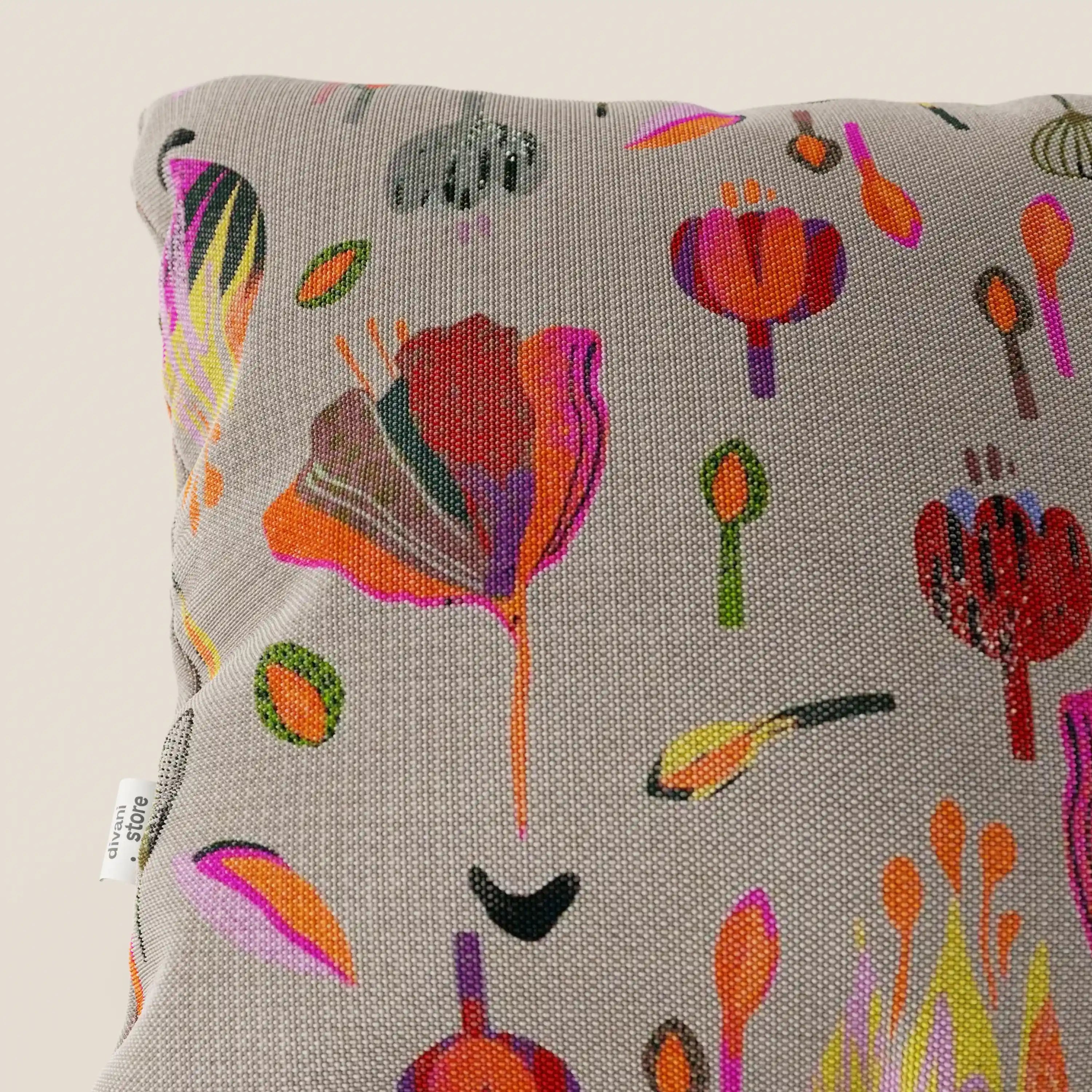 Primo piano del cuscino Joy 45x45 cm di Divani.Store, caratterizzato da un vivace motivo floreale astratto multicolore su un fresco tessuto di cotone grigio impermeabile. Sul bordo sinistro è visibile una piccola etichetta bianca.