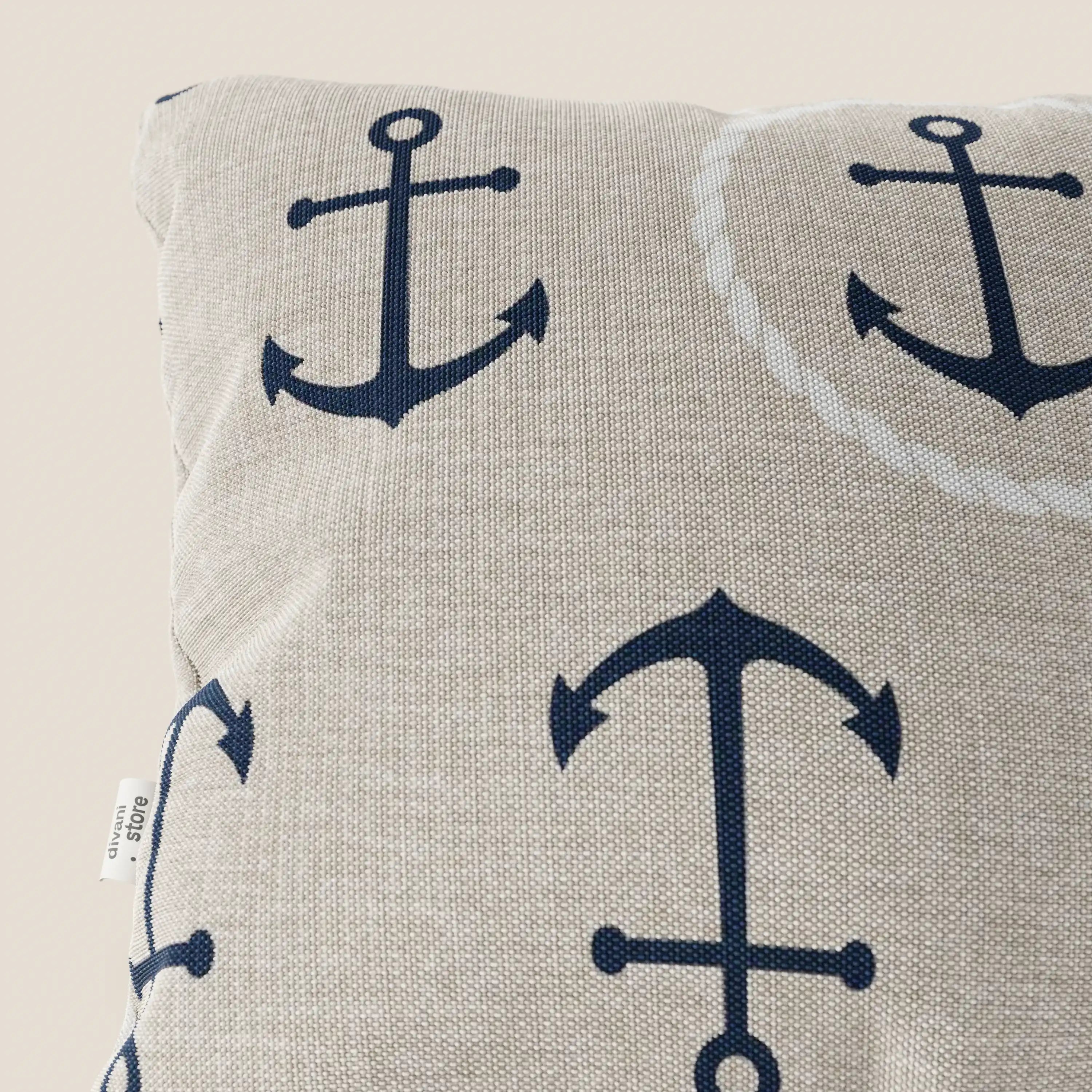 La collezione di cuscini Nautilus di Divani.Store è caratterizzata da un cuscino beige impermeabile con grandi ancore blu scuro, una piccola etichetta laterale bianca e un tessuto testurizzato lavabile. Solo una parte del cuscino in stile marino è visibile su uno sfondo chiaro.