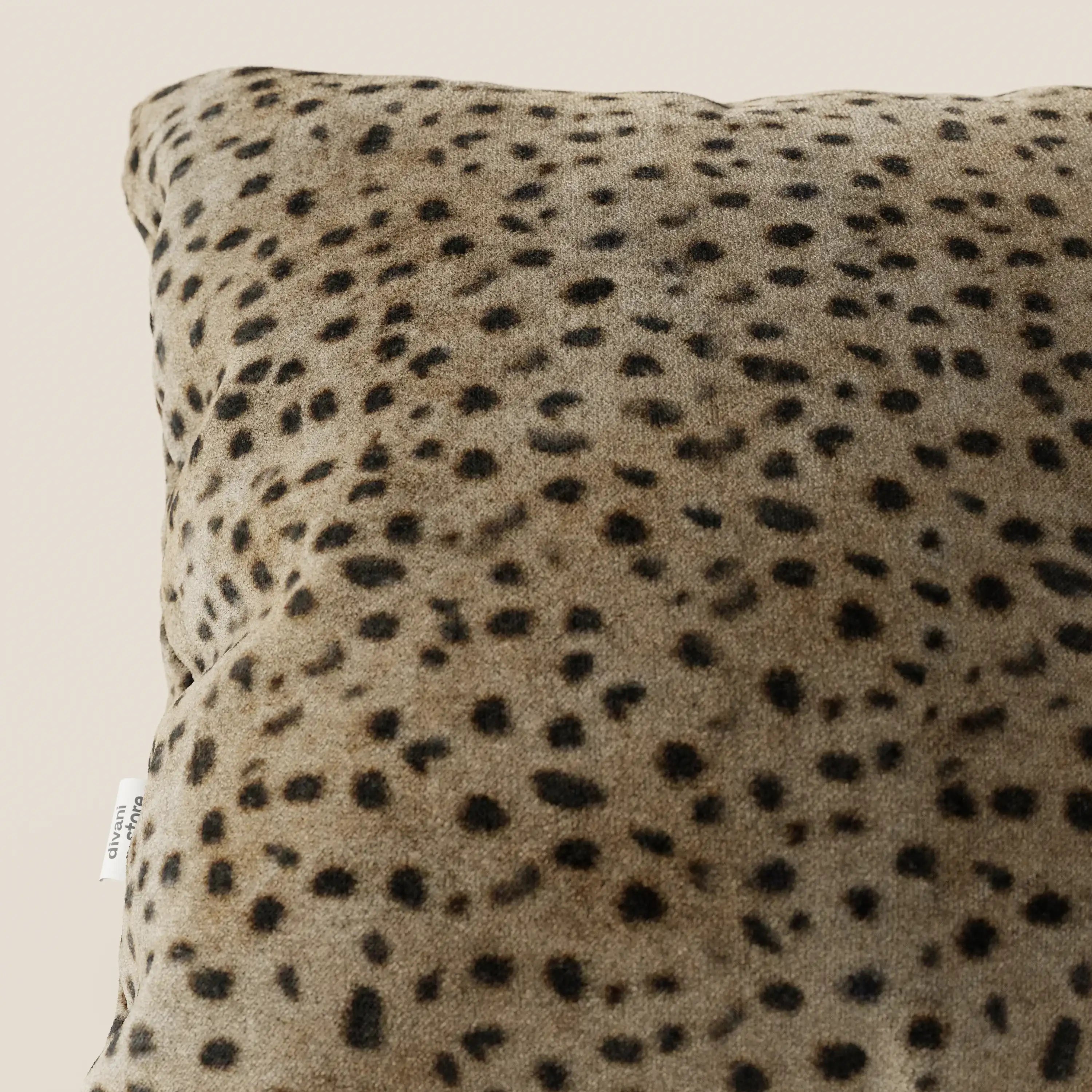 Primo piano del cuscino Wild 45x45 di Divani.Store della collezione Wild, in microfibra impermeabile con stampa ghepardo. Una piccola etichetta bianca si trova sul bordo inferiore sinistro, con uno sfondo beige chiaro.