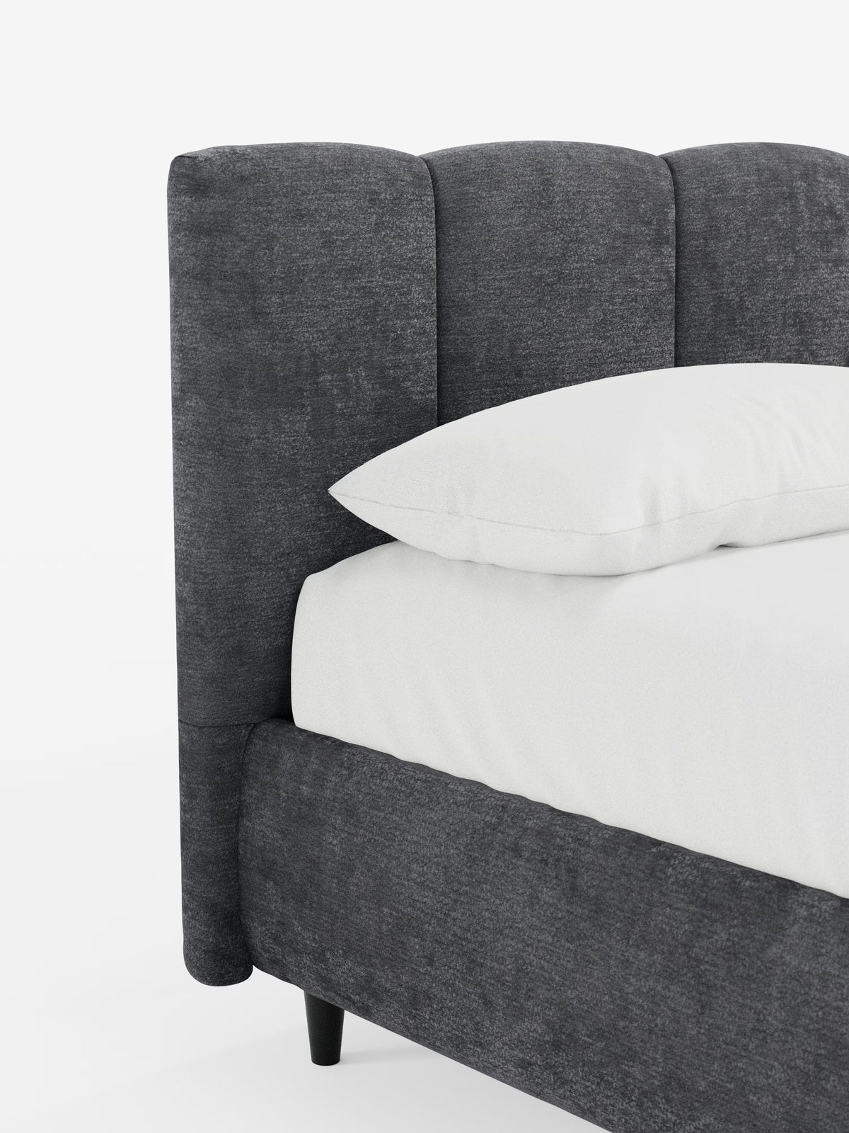 Un primo piano del letto imbottito ARKAM con contenitore e testiera a lavorazione verticale di Letti.store, caratterizzato da un design moderno in tessuto grigio scuro certificato Oeko-Tex®. La struttura imbottita in stile shabby chic presenta una testiera curva con dettagli verticali, abbinata a un materasso e a un cuscino bianchi. Il letto poggia su corte gambe nere su uno sfondo bianco a tinta unita.