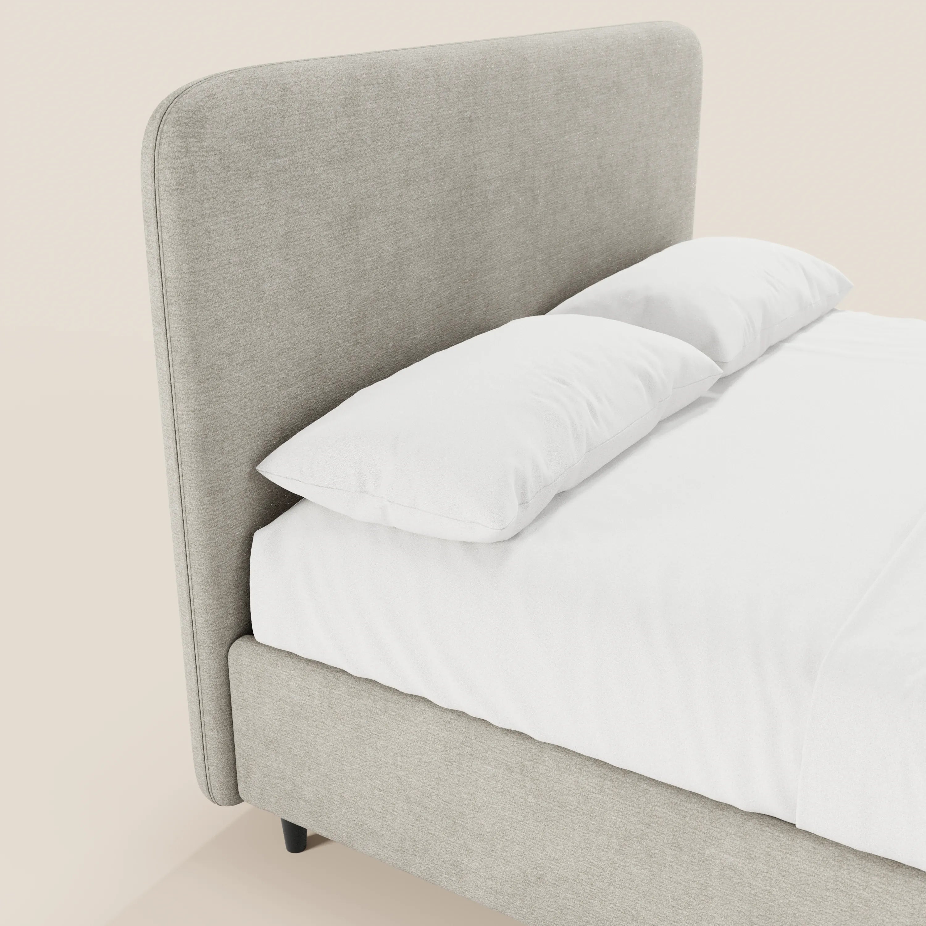 Il letto imbottito KAELOS minimal di Letti.store presenta una struttura rivestita in ciniglia grigio chiaro, una testiera alta e arrotondata, gambe alte e uno spazio contenitivo. Rivestito con lenzuola bianche e due cuscini, risalta su uno sfondo beige tenue.