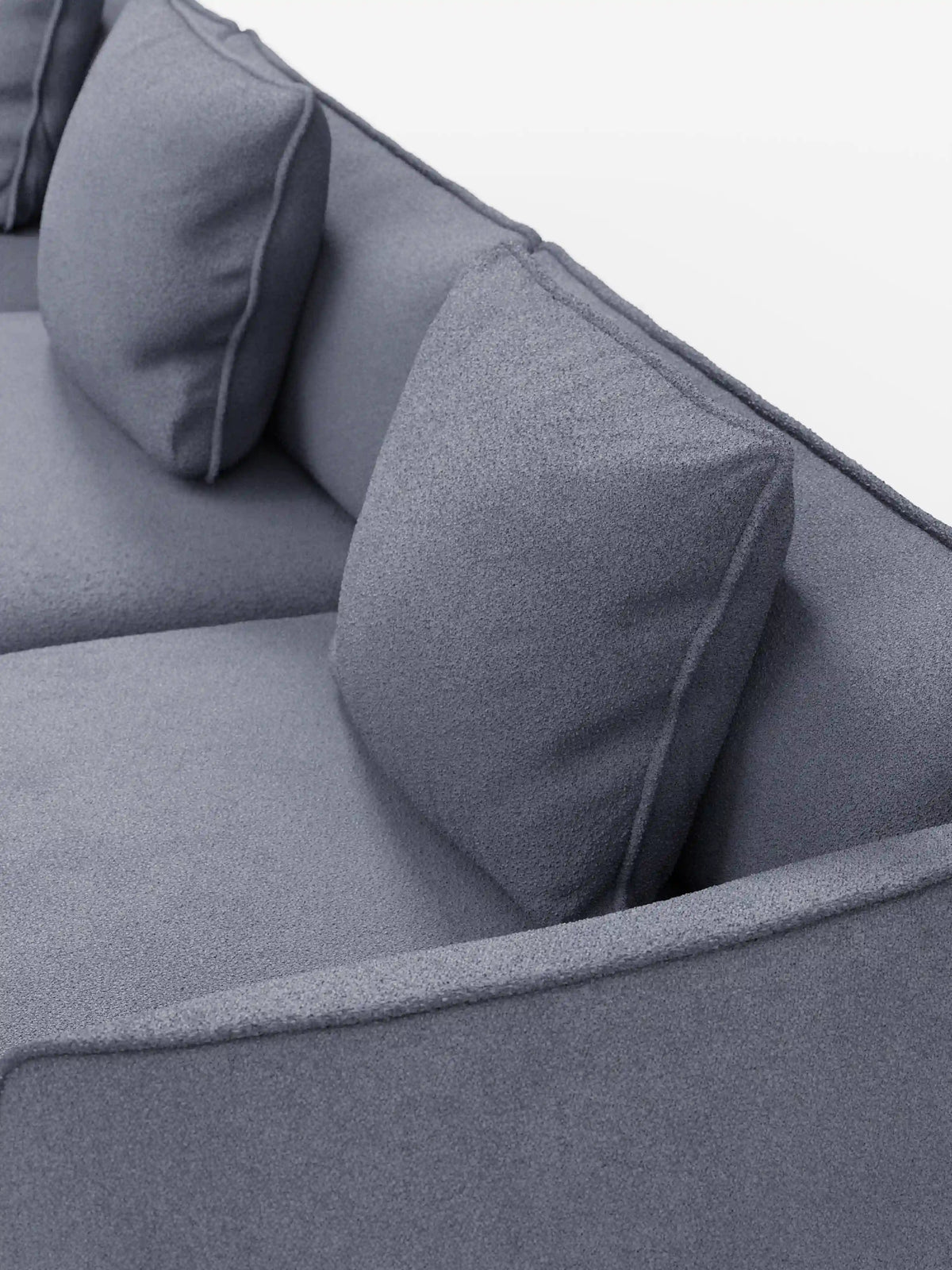Un primo piano del divano modulare a 3 posti “Nimbus” di Divani.Store, rivestito in morbido tessuto T33 effetto cotone resistente alle macchie. Il moderno design grigio presenta due cuscini di seduta e due cuscini quadrati abbinati con una finitura leggermente testurizzata. I braccioli e lo schienale a vista creano un look pulito e minimalista sullo sfondo bianco a tinta unita.