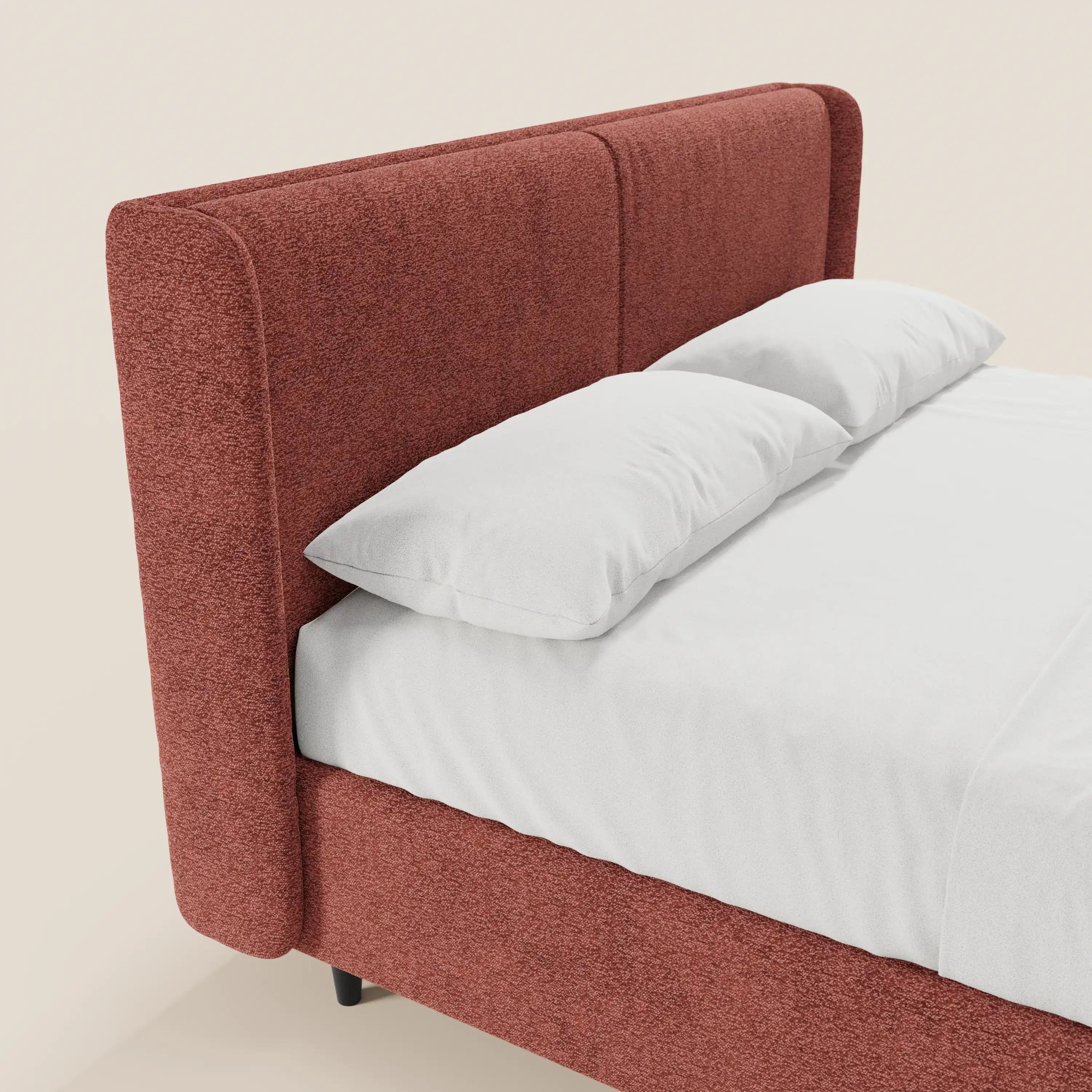 Il letto di design VALKIRIA di Letti.store presenta una testiera alta, rivestita in tessuto Oeko-Tex® color ruggine, con 2 cuscini imbottiti e una base contenitiva. Nell’immagine è raffigurato con un lenzuolo con angoli bianco e cuscini su uno sfondo chiaro; visibile solo in parte.