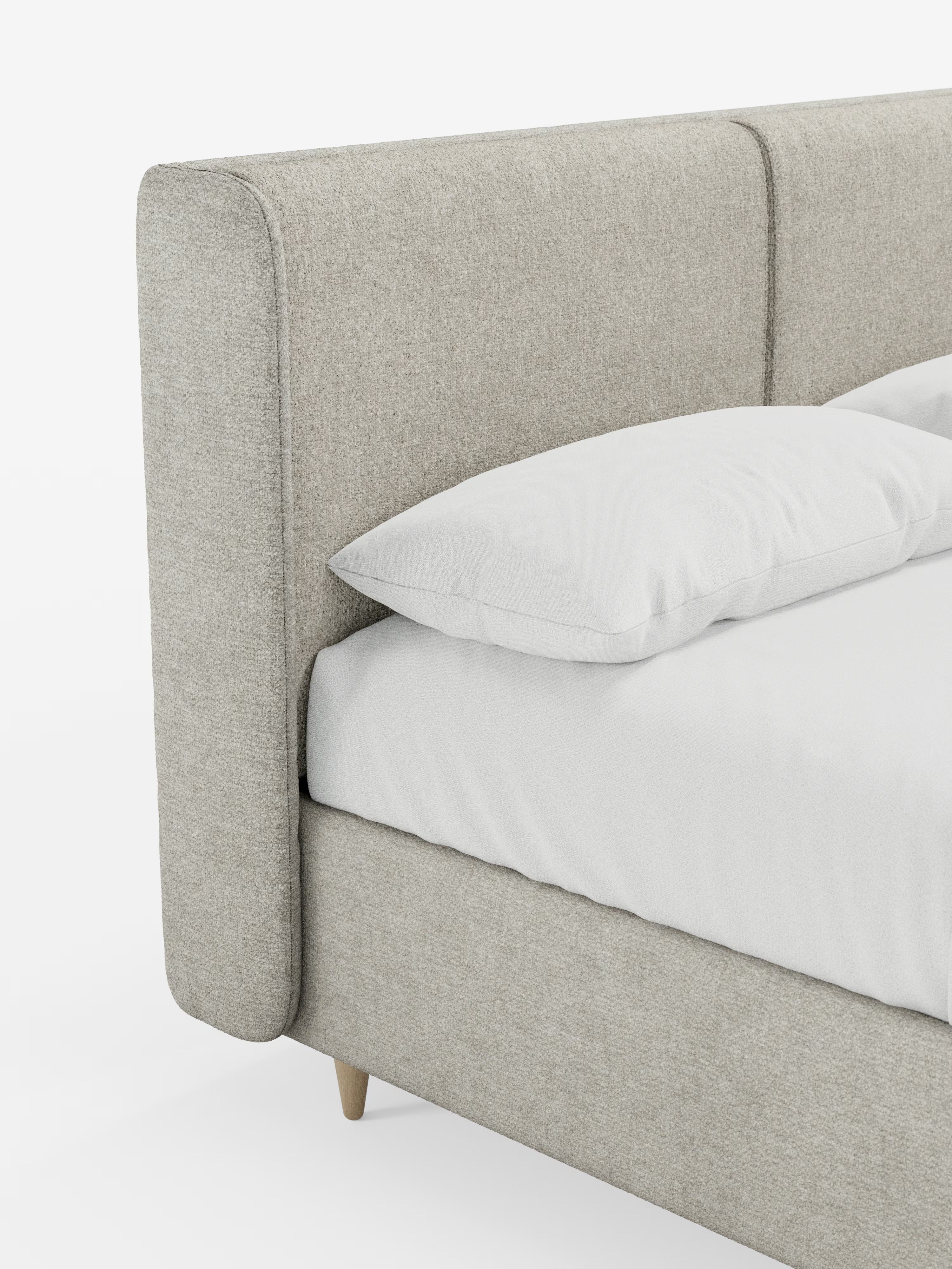 Un primo piano del letto imbottito bicolore con contenitore VALKIRIA di Letti.store ne mette in risalto il design moderno, con una struttura rivestita in grigio chiaro e una testiera imbottita, curva e avvolgente, per un comfort ancora maggiore. Il letto è dotato di cuscini schienali e robuste gambe in legno chiaro, ed è rivestito con lenzuola bianche e un cuscino bianco. Su uno sfondo bianco a tinta unita, spicca la semplice eleganza di questo modello di Letti.store.