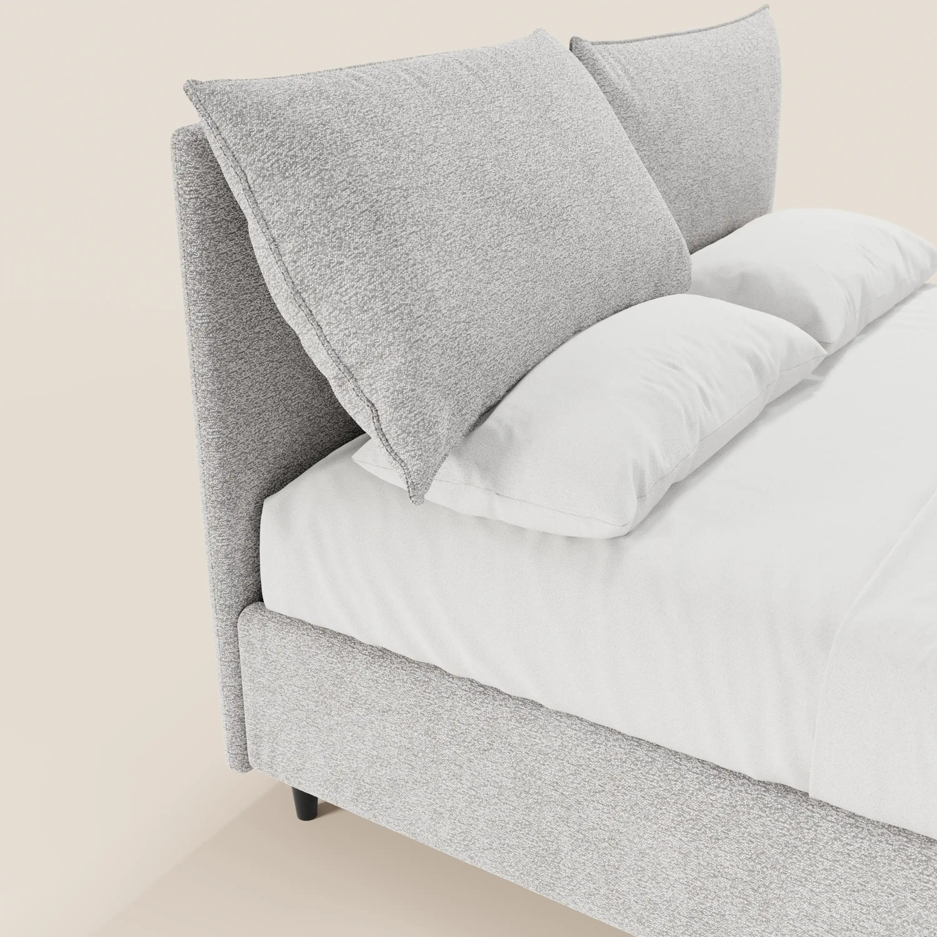 Un primo piano del letto imbottito ZAYRON di Letti.store, caratterizzato da una testiera e da una struttura in tessuto grigio chiaro certificato Oeko-Tex® con morbidi cuscini regolabili. Lenzuola bianchissime e due grandi cuscini grigi poggiano contro la testiera; lo sfondo è color crema chiaro.