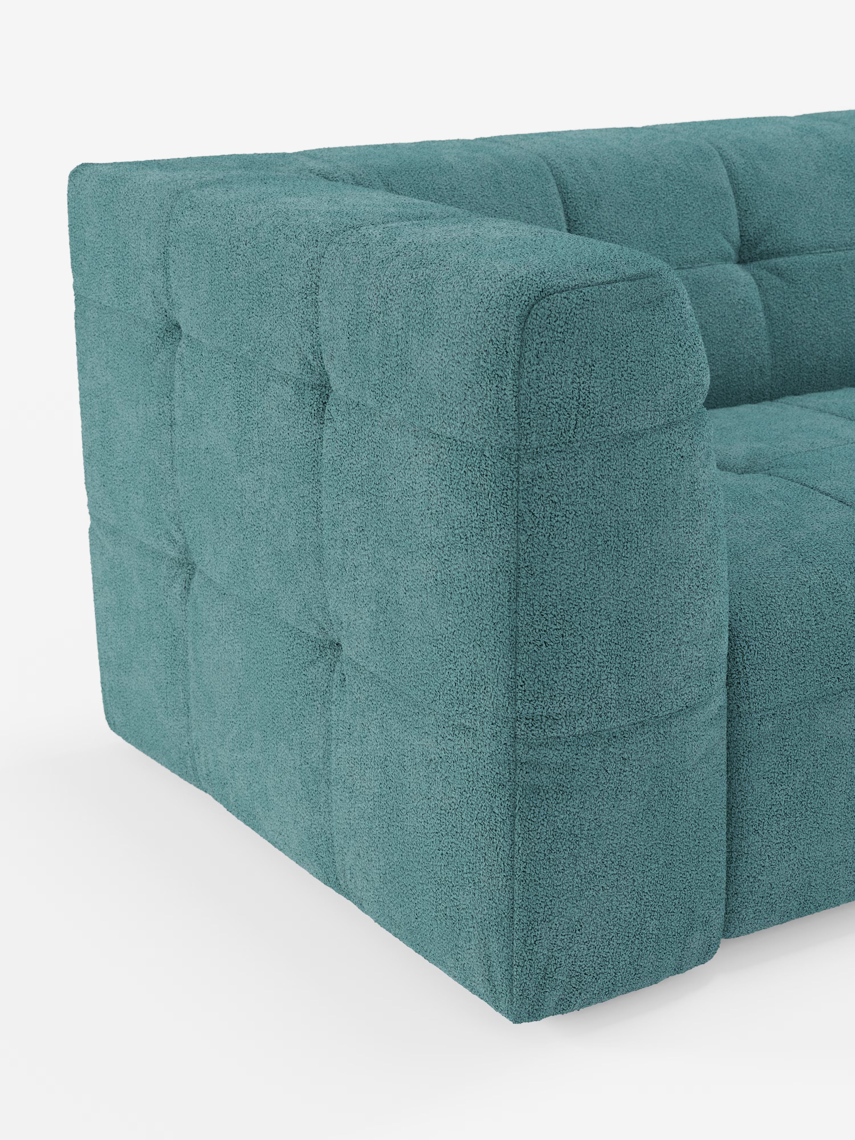 Primo piano di un divano moderno color verde acqua rivestito in tessuto bouclé dalla trama rigata. Questo divano moderno presenta una profonda trapuntatura a quadrati sui braccioli e sui fianchi, con cuscini morbidi e dalla forma squadrata. Lo sfondo bianco mette in risalto il colore e i dettagli del mobile.