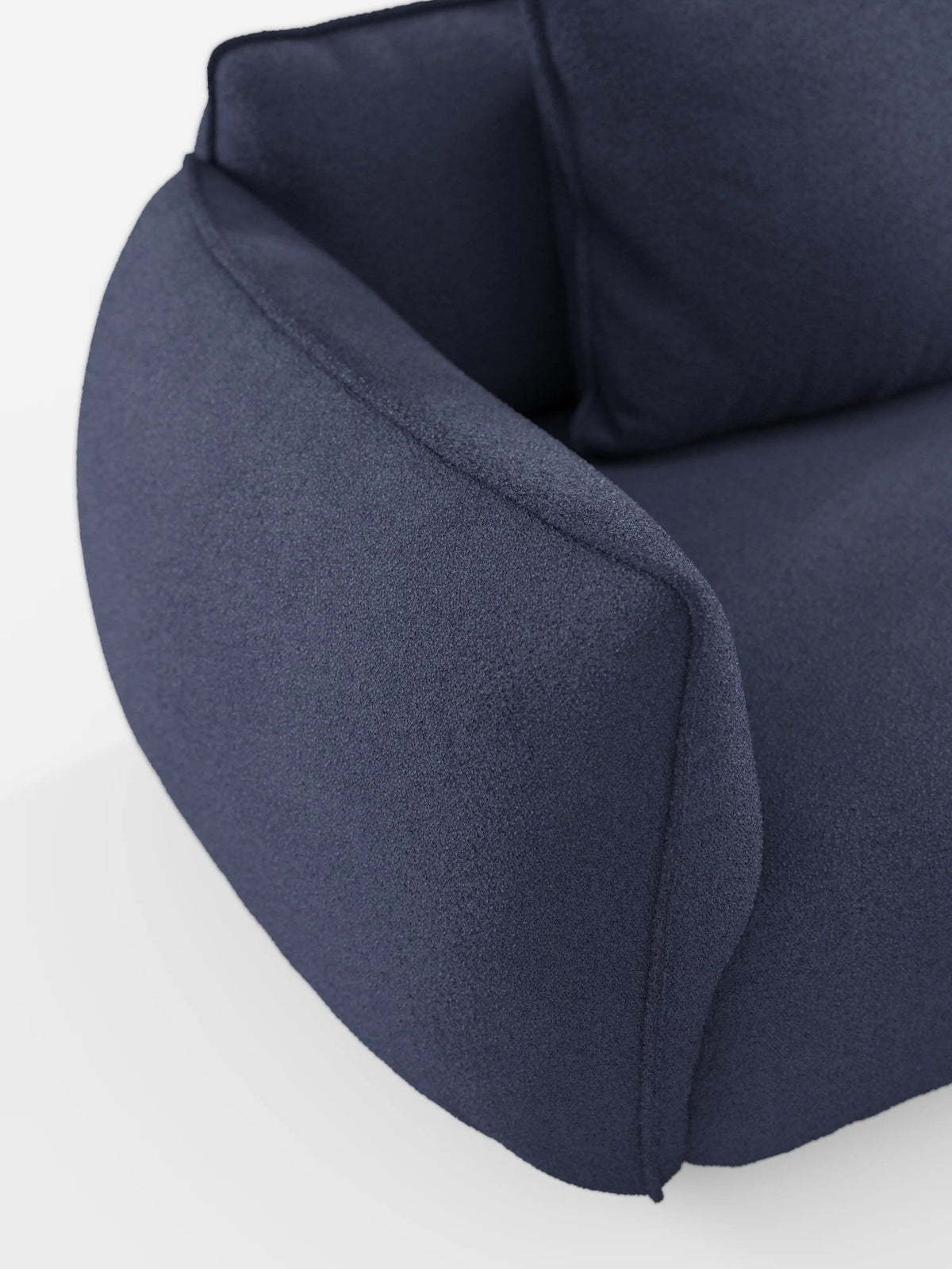 Primo piano del divano angolare con penisola Nimbus di Divani.Store, caratterizzato da braccioli e schienale morbidi e arrotondati. Questo moderno divano modulare è rivestito in tessuto T33 blu scuro effetto cotone, lavabile e dalla trama ruvida, con cuscini spessi e un design minimalista. Lo sfondo bianco mette in risalto le forme eleganti del divano e i dettagli del tessuto.