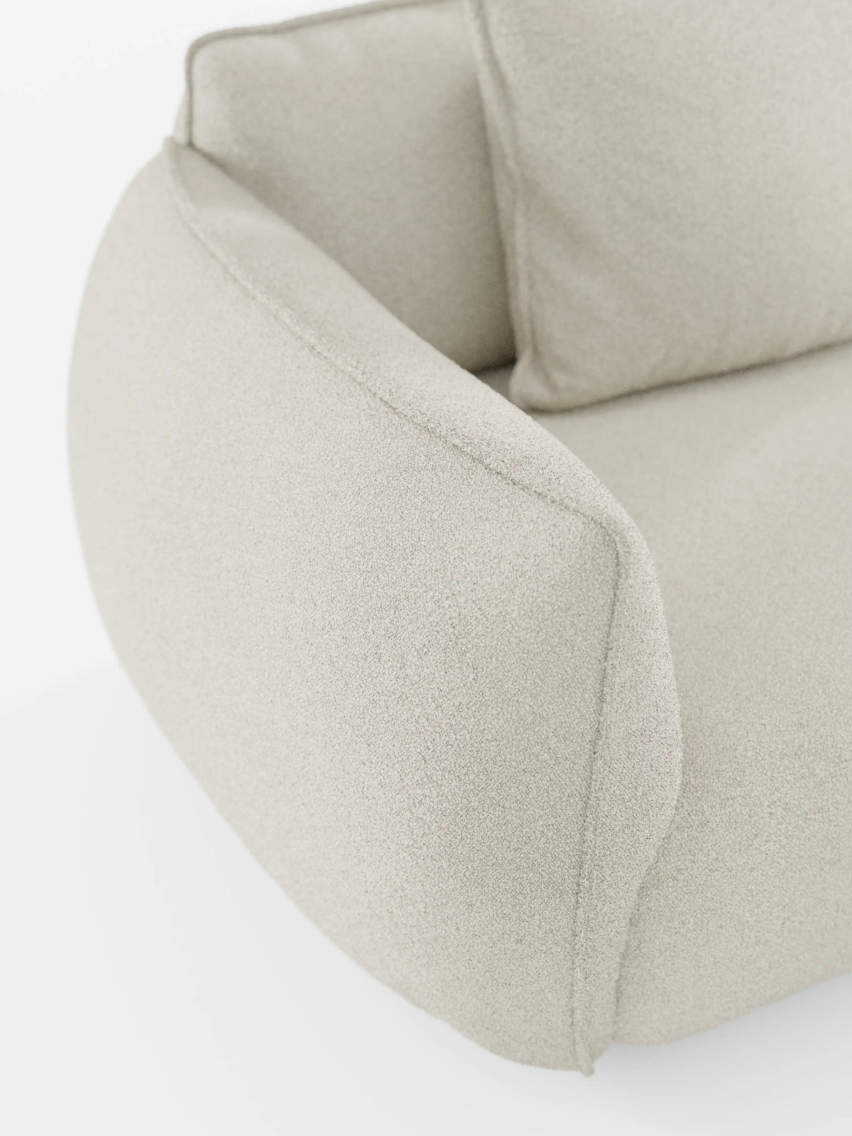 Primo piano del divano angolare con penisola componibile Nimbus di Divani.Store, rivestito in morbido tessuto T33 effetto cotone, resistente alle macchie, in beige chiaro. Questo moderno divano componibile presenta braccioli arrotondati e imbottiti e un cuscino coordinato, che trasmettono comfort e stile su uno sfondo bianco a tinta unita.