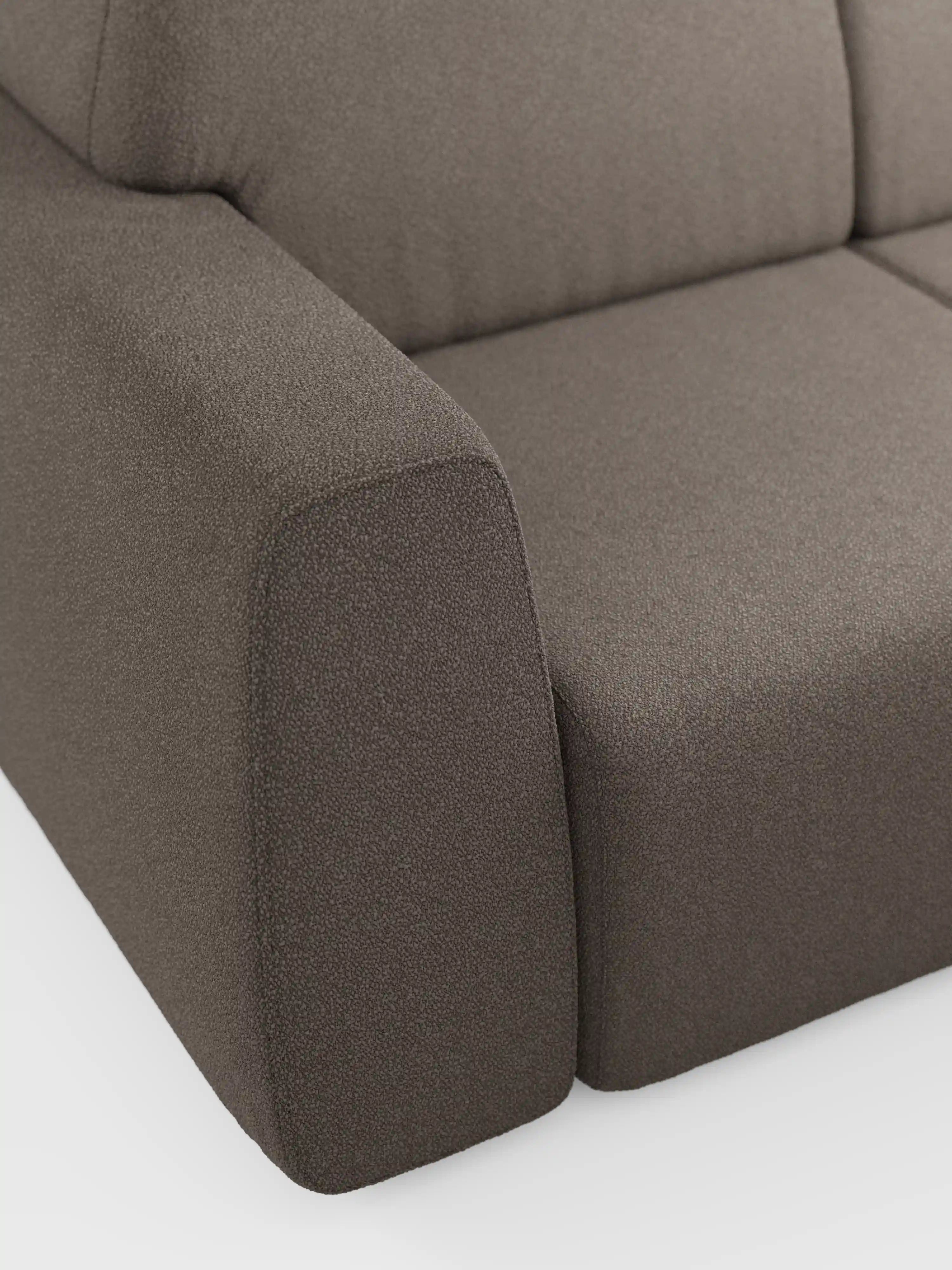 Primo piano del bracciolo sinistro e del cuscino di seduta del divano Orbit a 2 e 3 posti con sedute scorrevoli di Divani.Store, rivestito in tessuto smacchiabile effetto cotone T33. Il tessuto, fine e dalla trama marcata, presenta un aspetto simile al cotone, mentre i cuscini e il bracciolo sono morbidi e ben imbottiti. Lo sfondo è una superficie bianca e pulita.