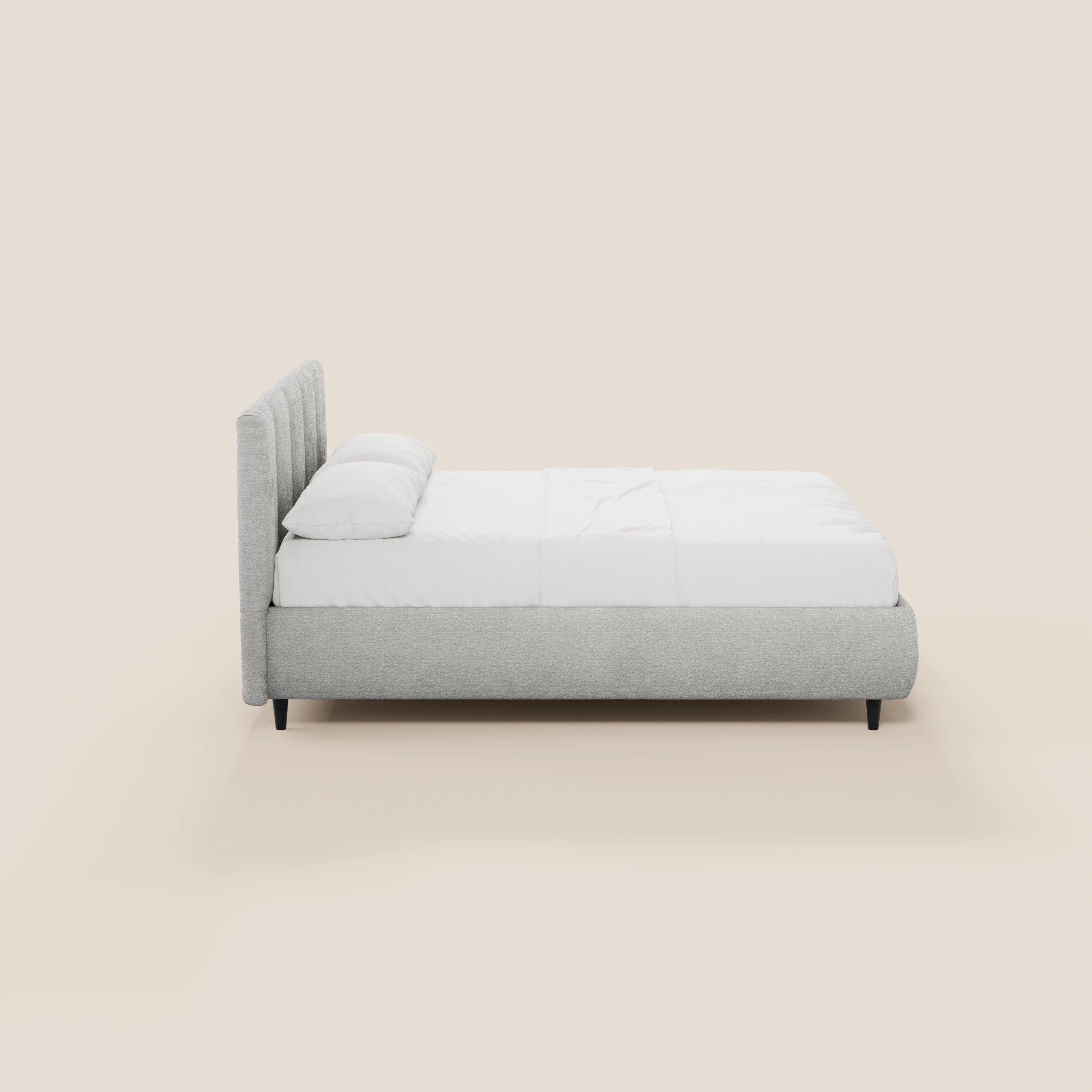 Il letto imbottito ARKAM di Letti.store presenta un design shabby chic in tessuto certificato Oeko-Tex®, con testiera cucita verticalmente e base contenitiva. Struttura grigio chiaro, materasso e cuscini bianchi, gambe nere, il tutto su uno sfondo beige.