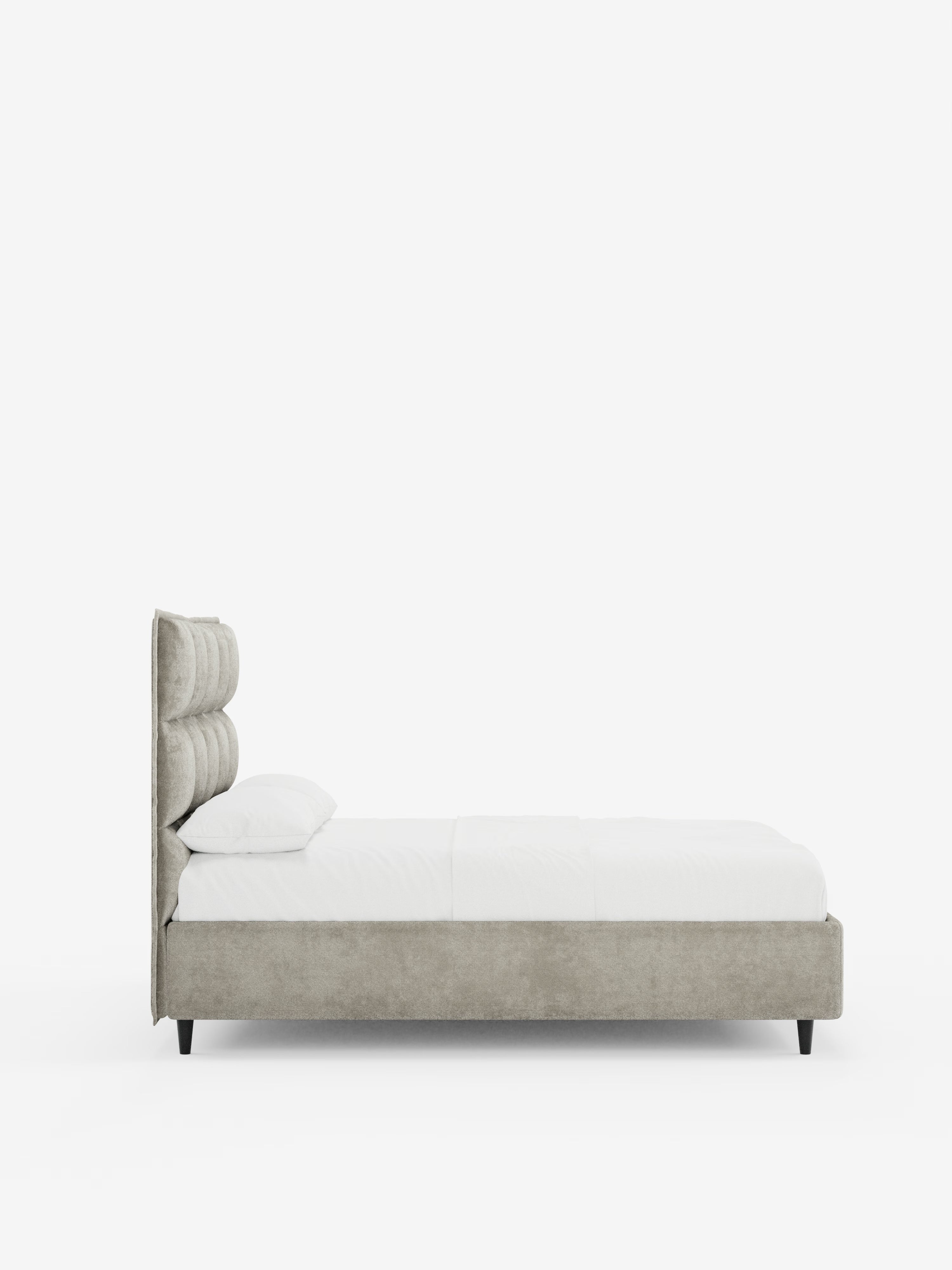Vista laterale del letto imbottito AURO con contenitore e testiera alta capitonné in ciniglia Oeko-Tex® di Letti.store, caratterizzato da una testiera alta con effetto capitonné e da un rivestimento in tessuto ciniglia grigio chiaro. Il letto è presentato in modo impeccabile con biancheria da letto bianca e un unico cuscino bianco, su uno sfondo bianco a tinta unita che ne esalta il design minimalista ed elegante.