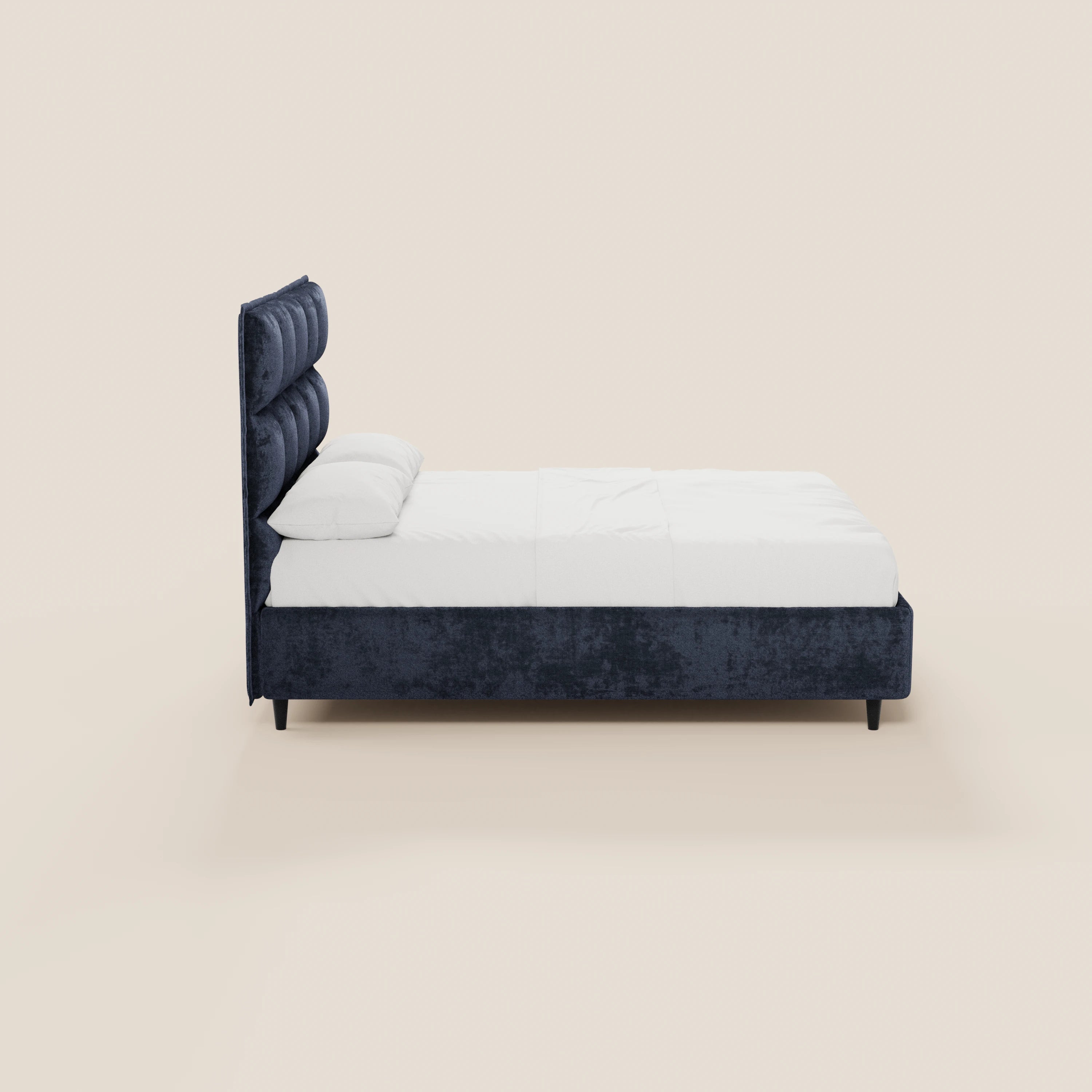 Vista laterale del letto imbottito AURO di Letti.store, caratterizzato da un’alta testiera capitonné in ciniglia blu scuro certificata Oeko-Tex®, con biancheria da letto bianca e due cuscini, su uno sfondo beige chiaro.