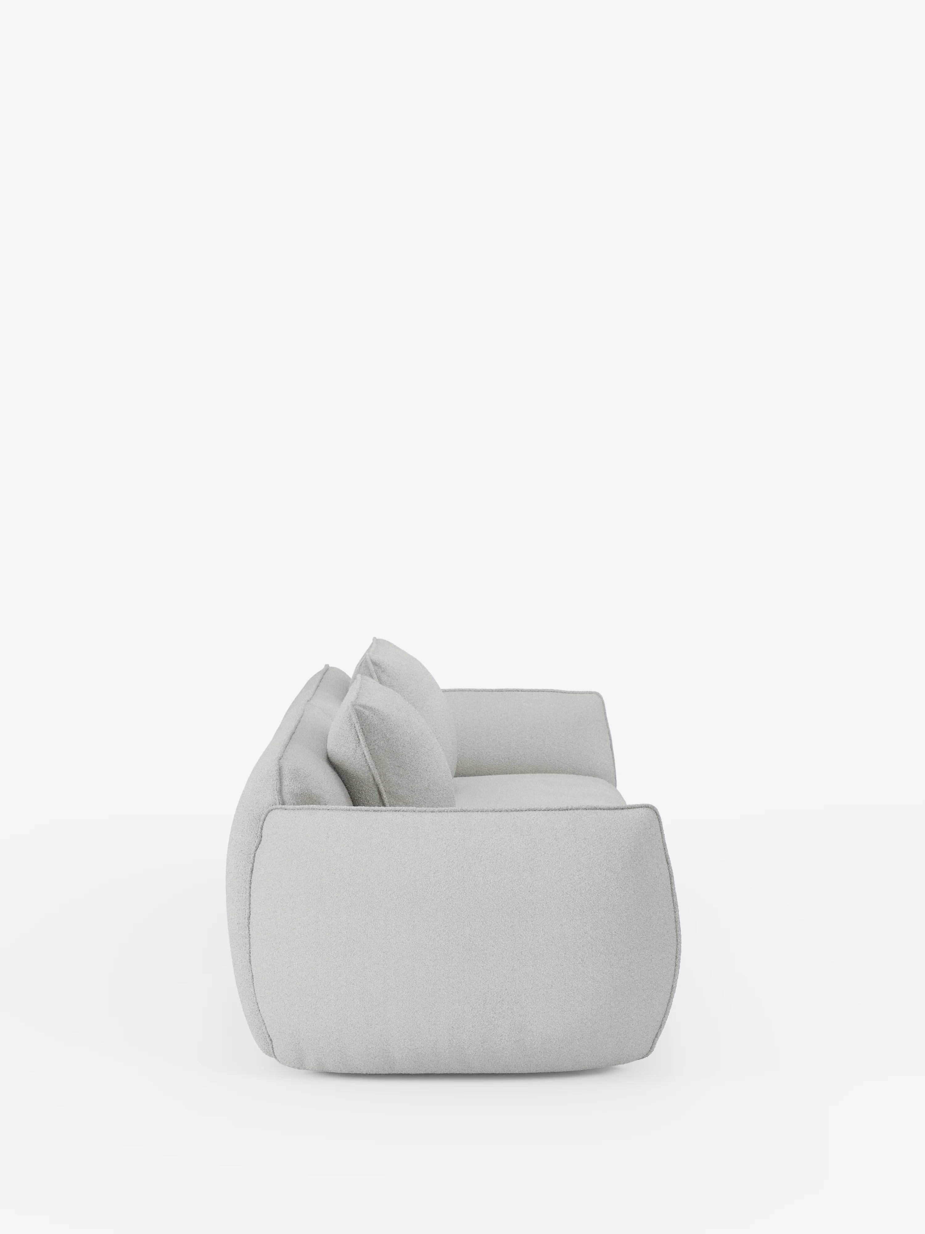 Vista laterale del divano modulare e componibile a 3 posti Nimbus da 250 cm di Divani.Store, rivestito in tessuto effetto cotone t33 grigio chiaro, resistente alle macchie e sfoderabile. Caratterizzato da due grandi cuscini dello schienale e un unico cuscino di seduta, questo divano moderno vanta un profilo basso e profondo con linee morbide e arrotondate che gli conferiscono un aspetto minimalista ma accogliente, in contrasto con uno sfondo bianco a tinta unita.