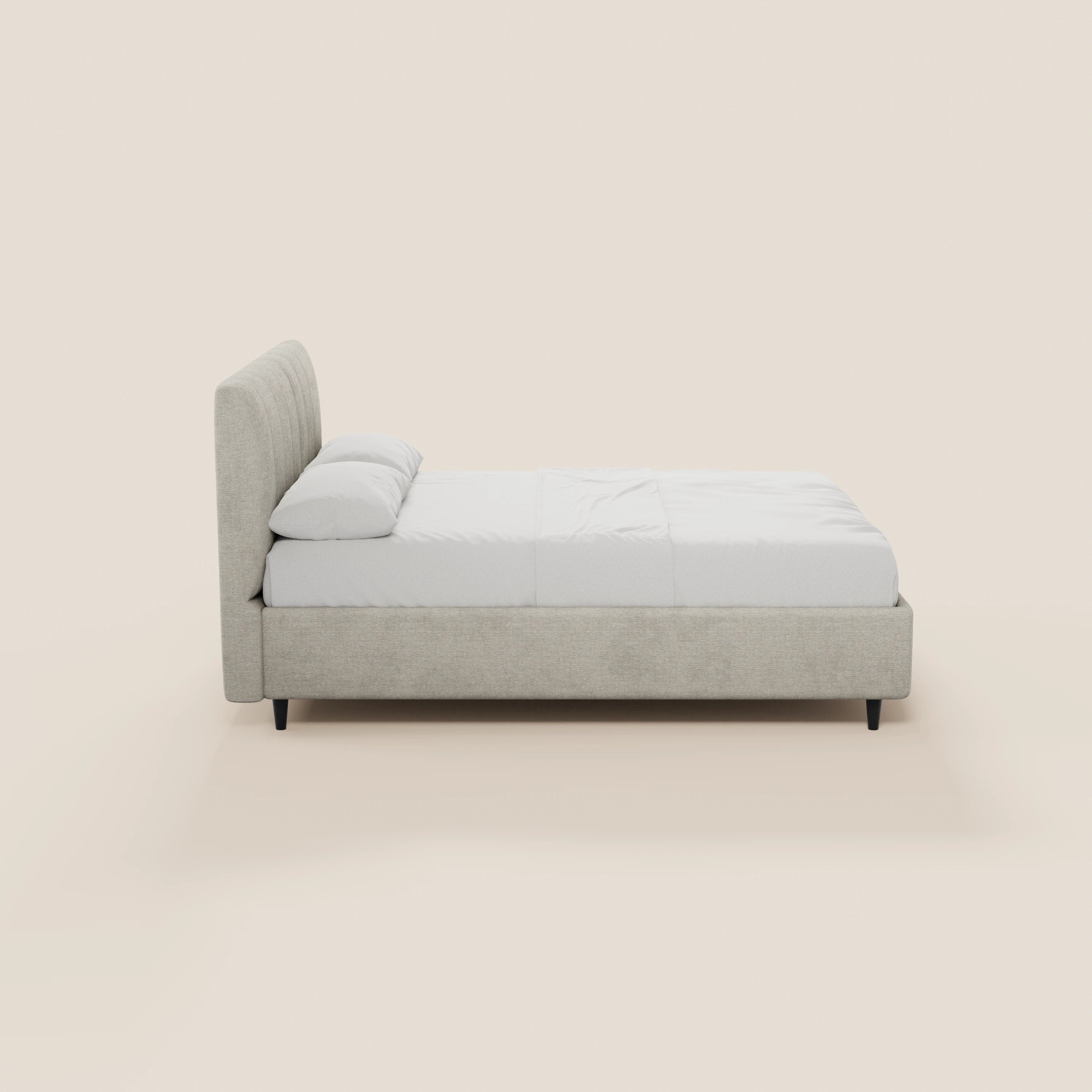 Il letto imbottito ONYX di Letti.store presenta un design minimalista con testiera in tessuto Oeko-Tex® beige chiaro con cuciture verticali, struttura imbottita, biancheria da letto bianca, due cuscini e gambe corte nere su uno sfondo bianco sporco.