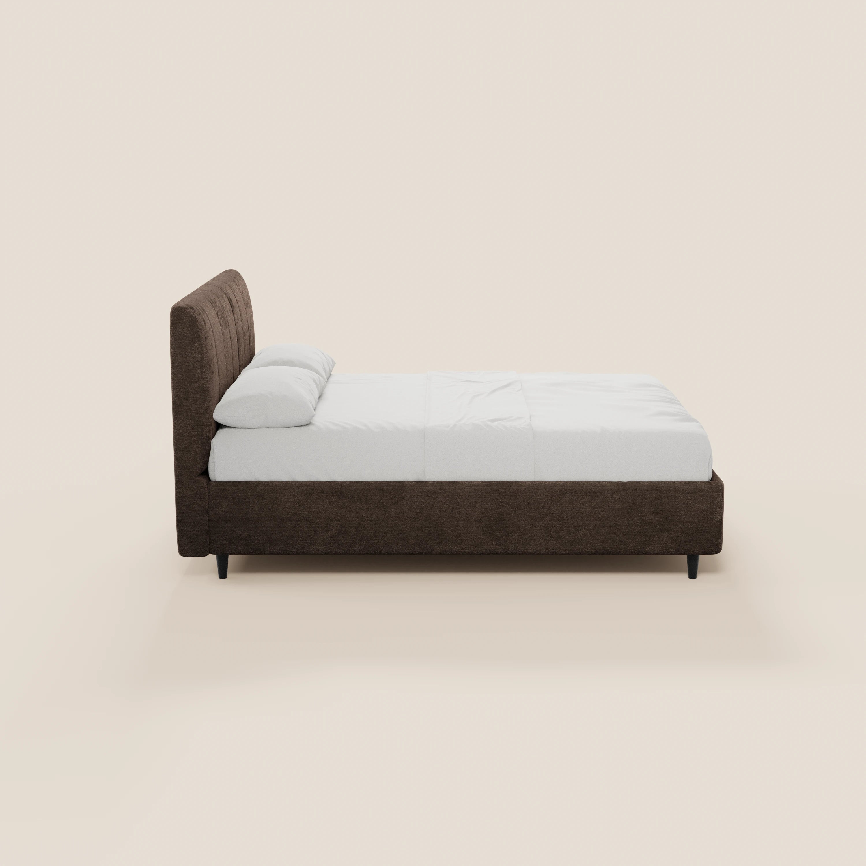 Vista laterale del letto imbottito ONYX con contenitore e testiera verticale in tessuto Oeko-Tex® di Letti.store, caratterizzato da una testiera marrone scuro, struttura imbottita, biancheria da letto bianca, due cuscini bianchi, gambe nere e uno sfondo beige chiaro.
