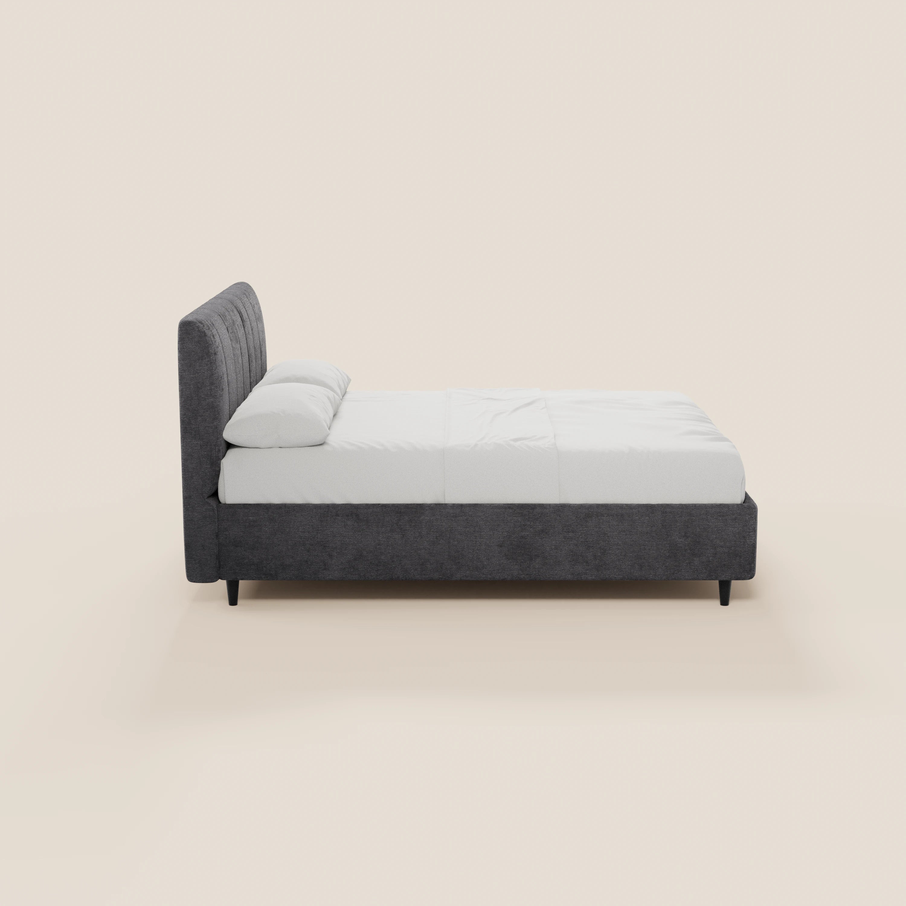 Una vista laterale del letto imbottito ONYX di Letti.store, realizzato in tessuto grigio scuro certificato Oeko-Tex®, caratterizzato da un'alta testiera verticale e da gambe corte nere. Il letto è rifatto con cura con biancheria da letto bianca e due cuscini, su uno sfondo beige chiaro.