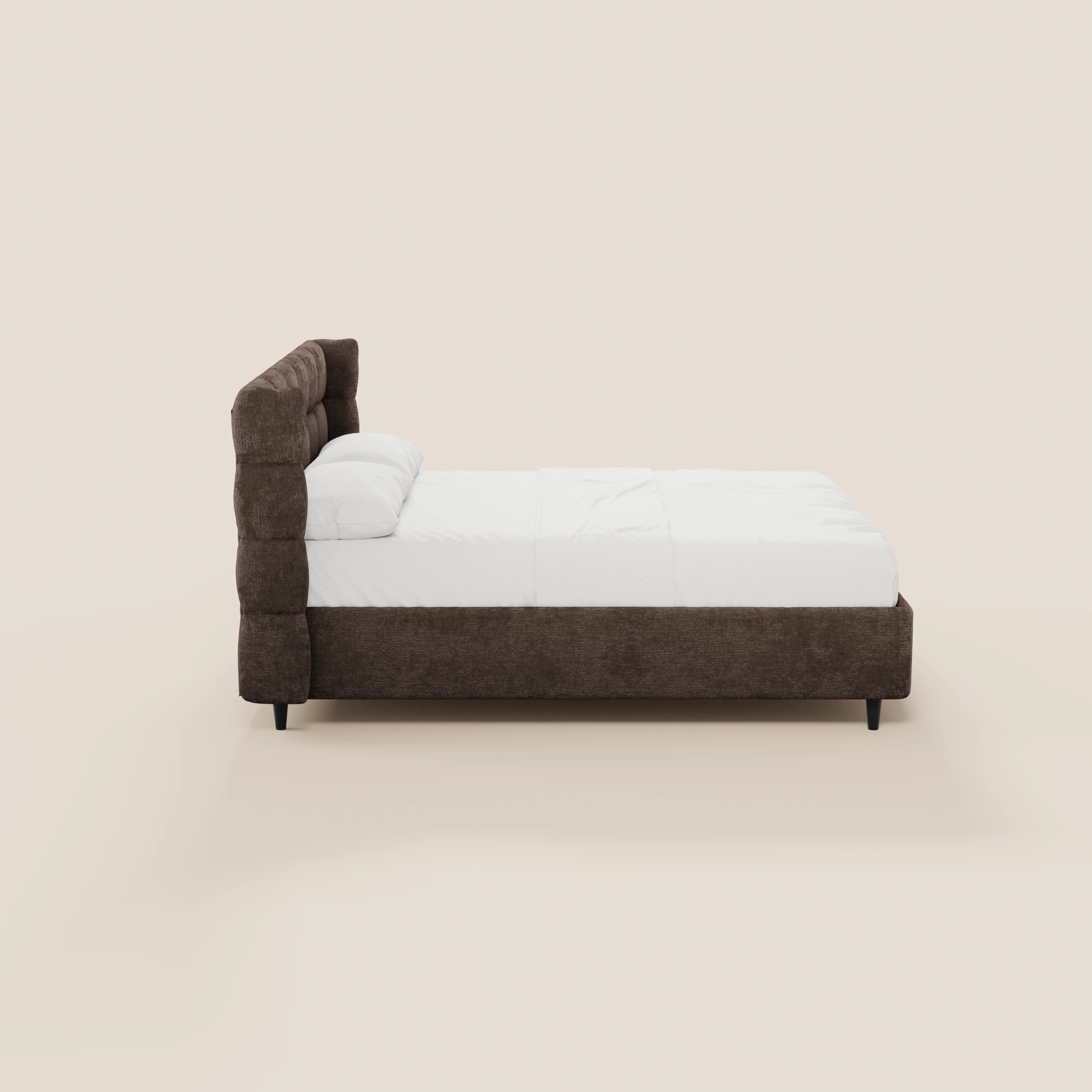 Una vista laterale del modello RAGNAR di Letti.store: un elegante letto imbottito con contenitore, testiera capitonné avvolgente in tessuto Oeko-Tex®, rivestimento marrone, biancheria da letto bianca, due cuscini e gambe nere su uno sfondo beige chiaro.