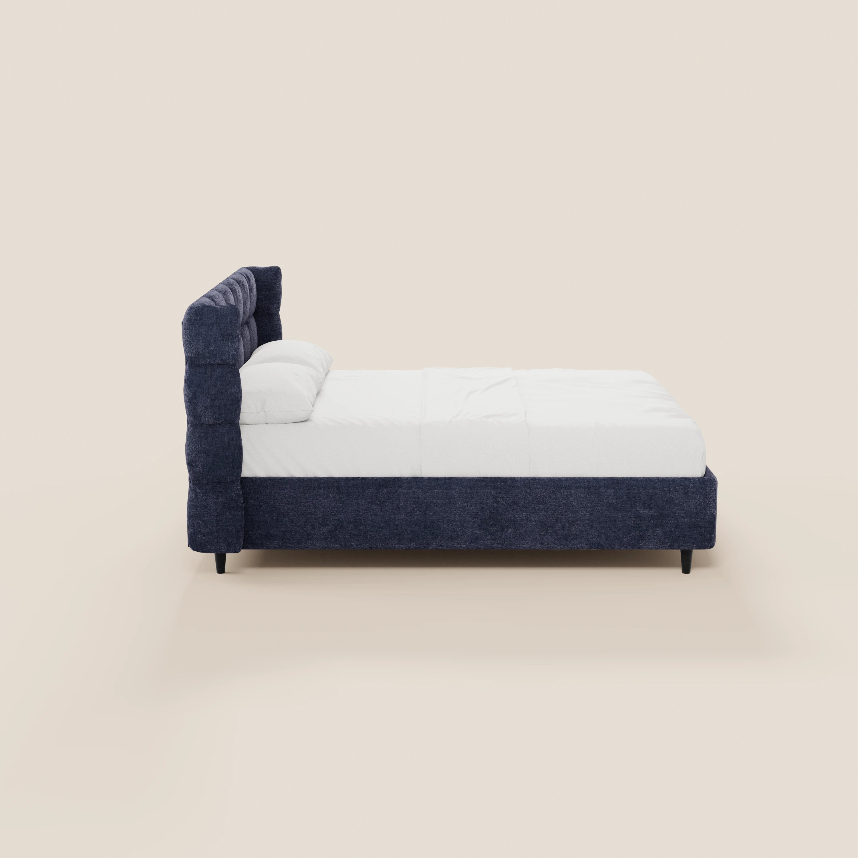 Una vista laterale del letto imbottito RAGNAR di Letti.store, dotato di vano contenitore e testiera capitonné avvolgente in tessuto blu scuro certificato Oeko-Tex®, con biancheria da letto bianca e gambe nere, su uno sfondo beige chiaro.