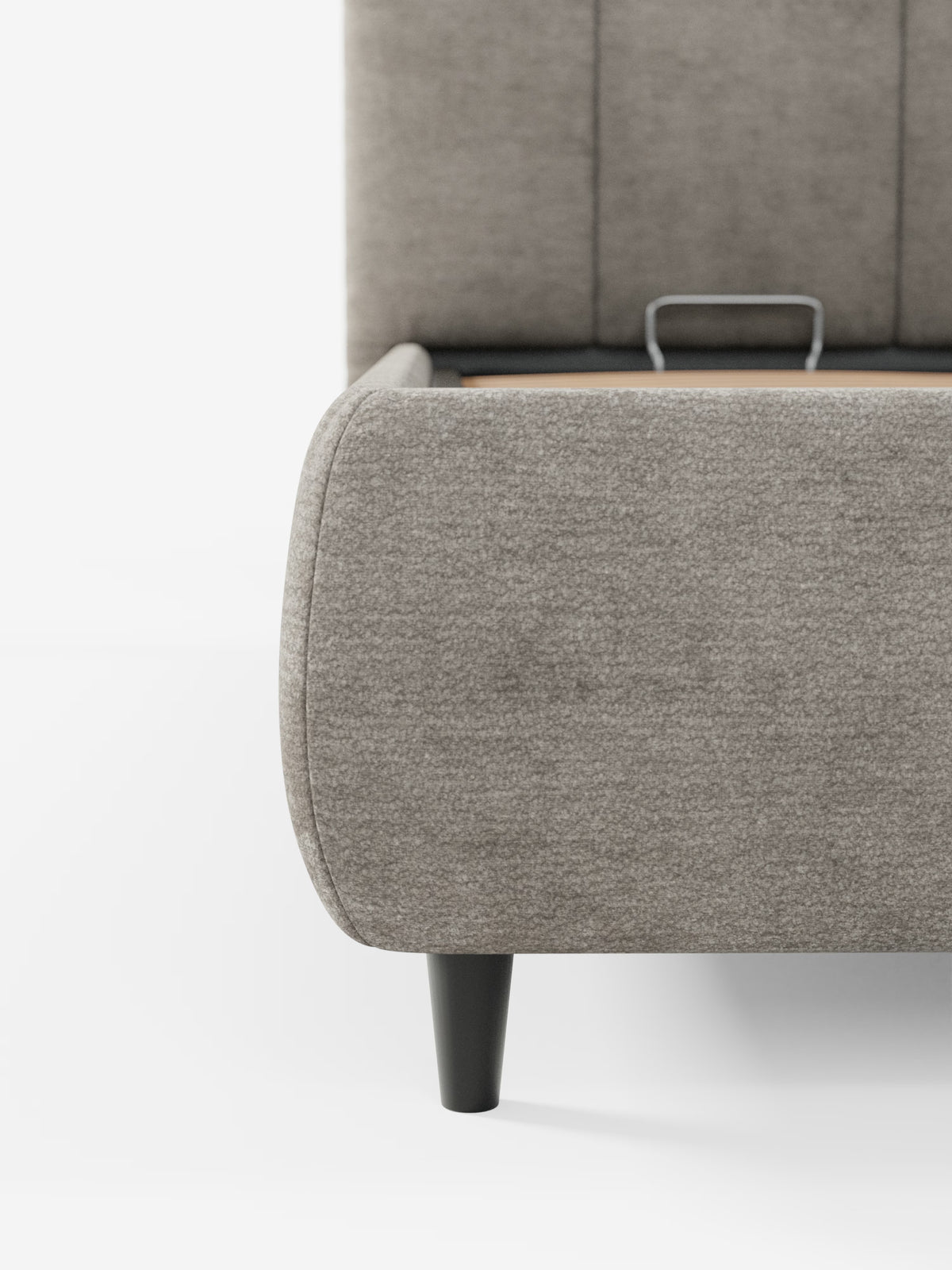 Un primo piano dell'angolo del letto imbottito ARKAM con contenitore e testiera a lavorazione verticale di Letti.store, caratterizzato da un tessuto grigio certificato Oeko-Tex® e da gambe nere. L'immagine mette in risalto una parte della testiera imbottita con cuciture verticali e un cassetto leggermente aperto con maniglia a vista integrata nella struttura del letto, il tutto su uno sfondo bianco a tinta unita.