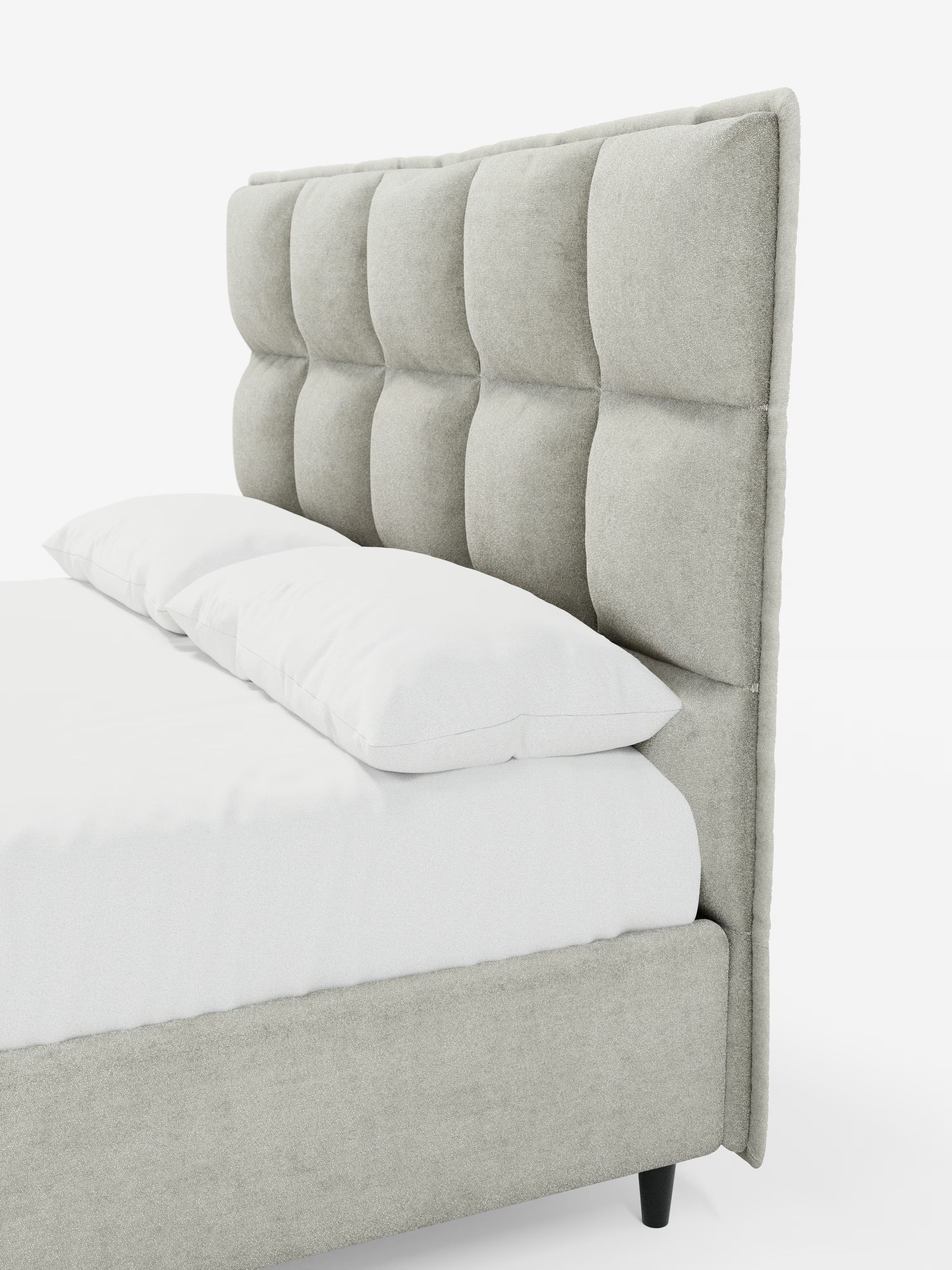 Il letto imbottito AURO con contenitore e testiera alta capitonné in ciniglia Oeko-Tex® di Letti.store è un letto imbottito grigio chiaro caratterizzato da una testiera alta con ampie sezioni quadrate imbottite che creano un elegante effetto capitonné. Il morbido rivestimento in tessuto ciniglia esalta il comfort del design. Nell’immagine, con biancheria da letto bianca e gambe nere, sono visibili solo una parte del materasso e due cuscini su uno sfondo bianco a tinta unita.