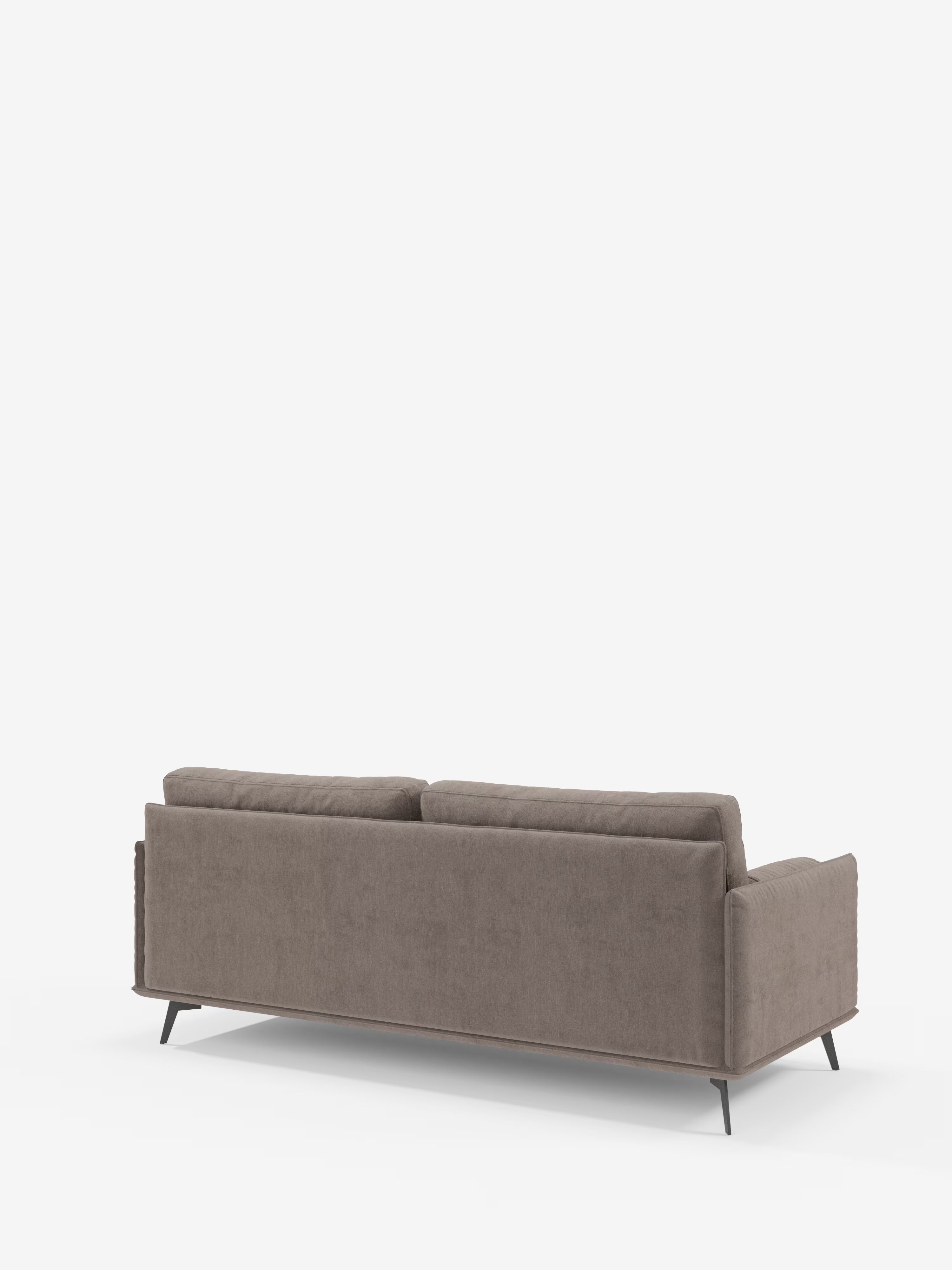 Il divano Basalto, modello lineare a 2 o 3 posti con seduta unica e base in metallo, rivestito in tessuto smacchiabile T31 di Divani.Store, è qui raffigurato visto da dietro. Questo divano moderno, di colore taupe, presenta due grandi cuscini dello schienale, braccioli dritti e gambe angolari in metallo nero. Sullo sfondo bianco a tinta unita, il design minimalista del divano risalta chiaramente.