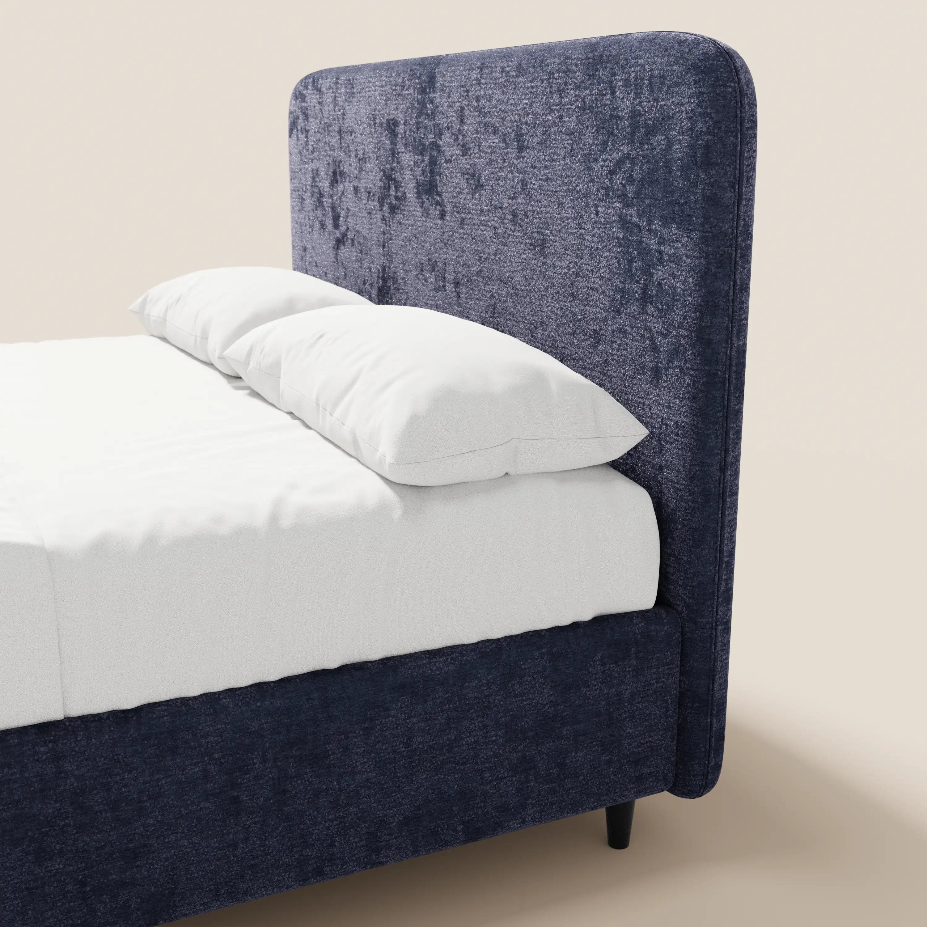 Una vista laterale ravvicinata del letto imbottito ONYX con contenitore e testiera verticale in tessuto Oeko-Tex® di Letti.store. Presentato in blu navy scuro, rifinito con cura con lenzuola e cuscini bianchi, poggia su gambe scure su uno sfondo beige chiaro.