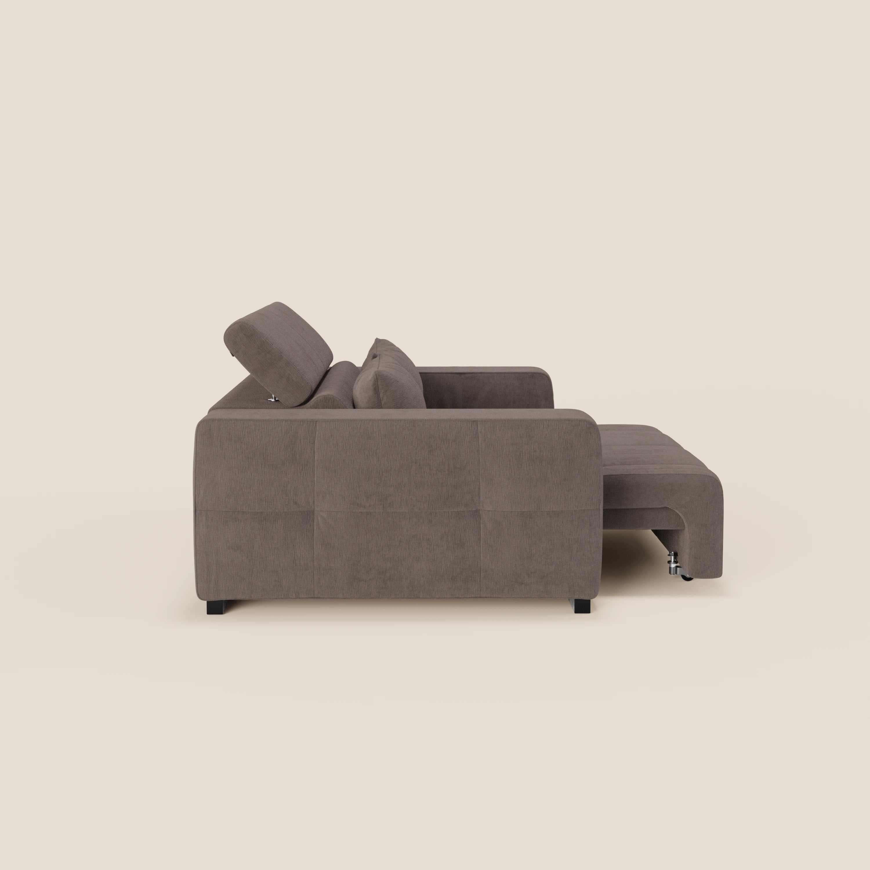Il Monarch Divano con Relax Elettrico di Divani.Store in tessuto smacchiabile T31 è presentato nella vista laterale con poggiatesta reclinabile in alto, chaise longue a destra, design moderno e squadrato, gambe basse nere e sfondo beige chiaro.