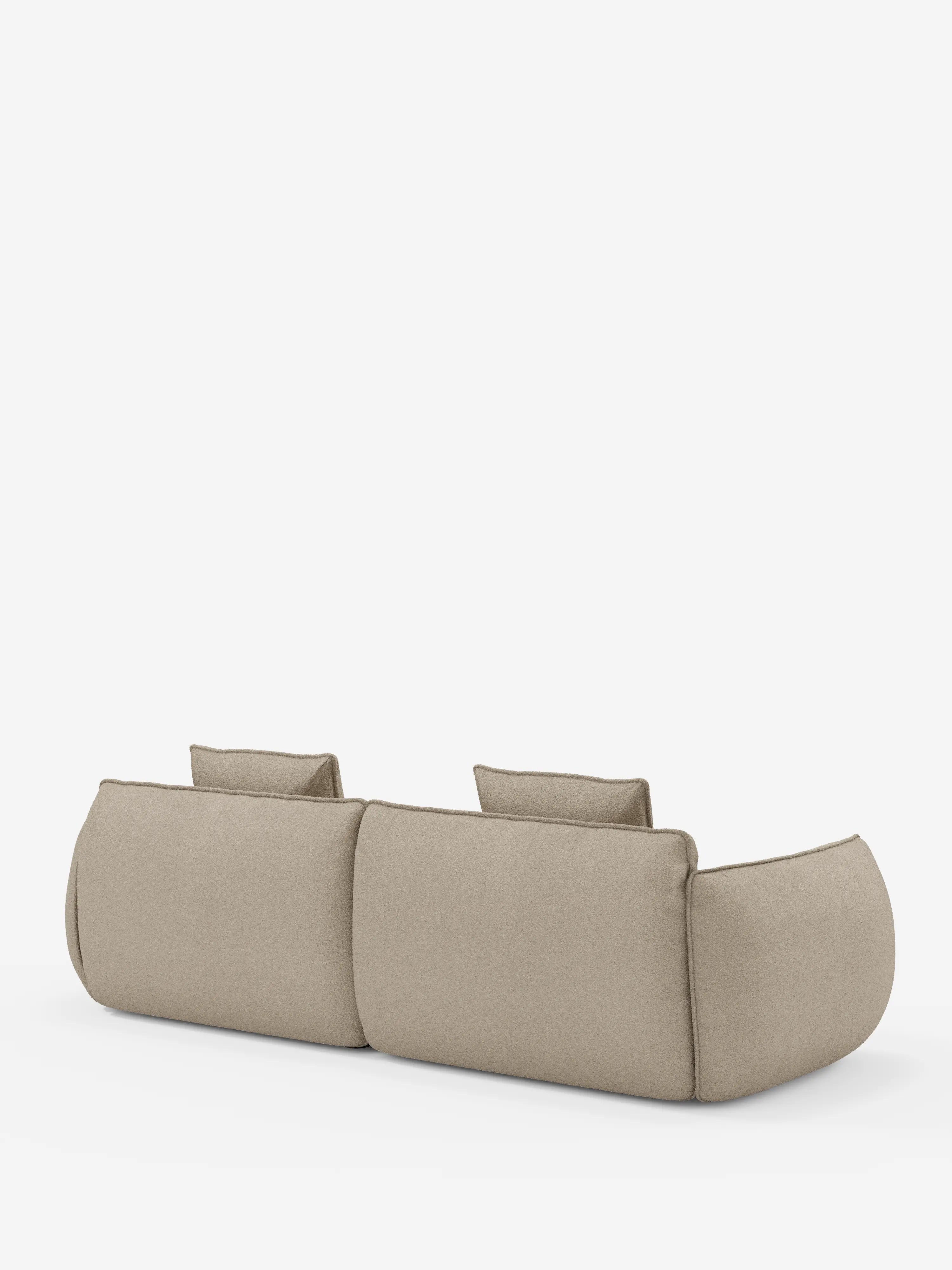 Un divano Nimbus contemporaneo a 3 posti, modulare e componibile da 250 cm di Divani.Store, rivestito in tessuto beige chiaro effetto cotone antimacchia (tessuto smacchiabile effetto cotone t33), è ripreso da dietro su uno sfondo bianco a tinta unita. Il divano modulare presenta due schienali, bordi arrotondati e una silhouette morbida e imbottita, senza gambe a vista, per un design minimalista.