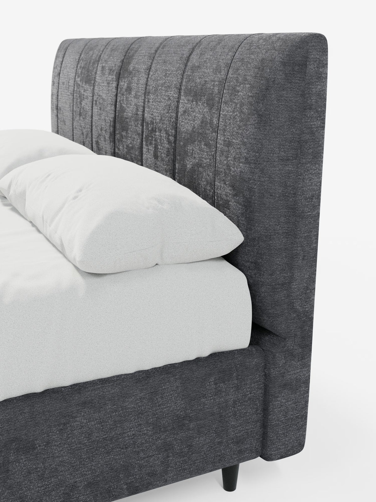Un primo piano del letto imbottito ONYX con contenitore e testiera verticale in tessuto certificato Oeko-Tex® di Letti.store mostra l'angolo della testiera grigio scuro, con cuciture verticali, e la struttura imbottita abbinata. Il letto contenitore è abbinato a un materasso e a un cuscino bianchi, su uno sfondo bianco a tinta unita.
