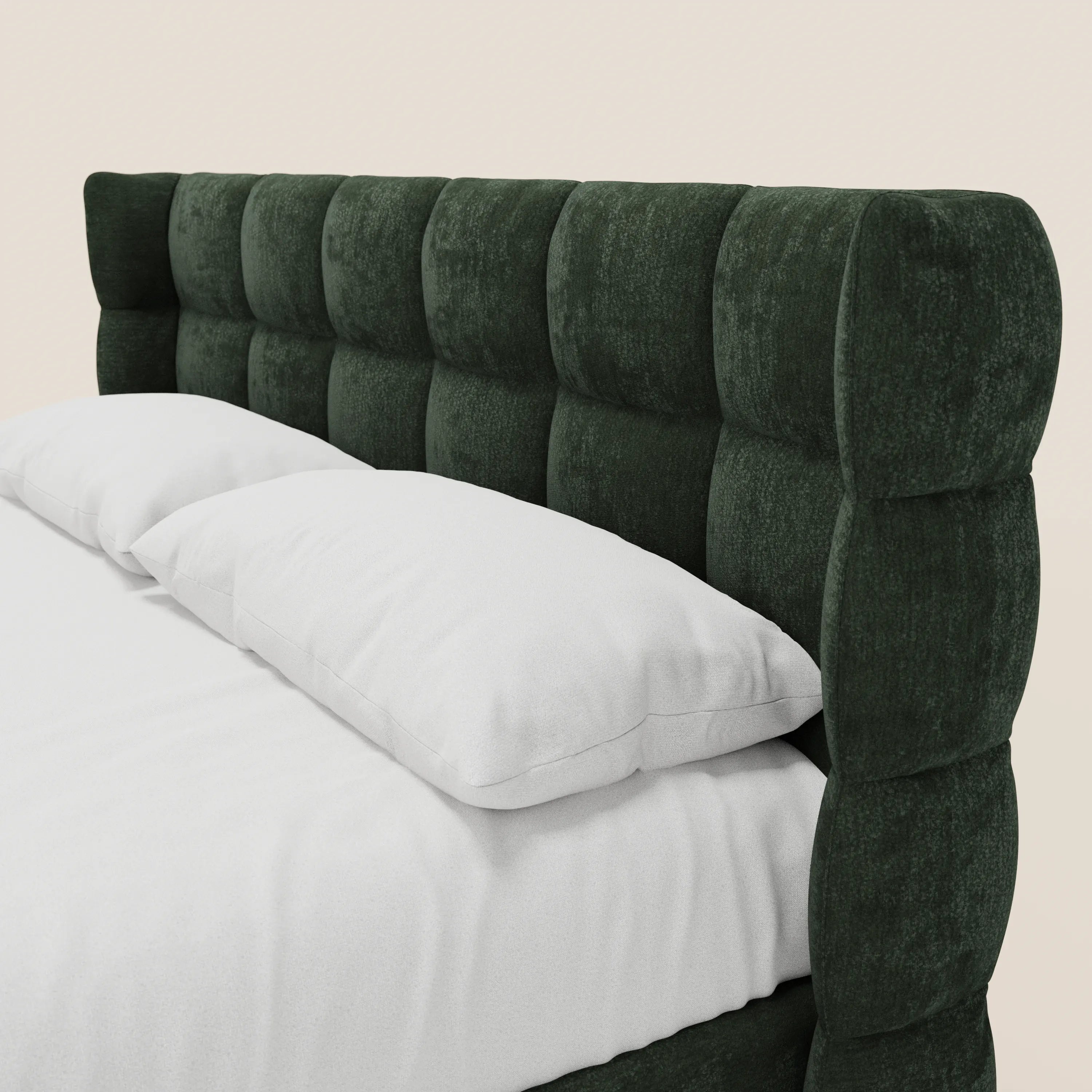 Un primo piano del letto imbottito RAGNAR di Letti.store mette in risalto la testiera rivestita in verde scuro con lavorazione capitonné, caratterizzata da ampi e morbidi quadrati in tessuto certificato Oeko-Tex®. Il letto è presentato con lenzuola e cuscini bianchi su uno sfondo a tinta unita.