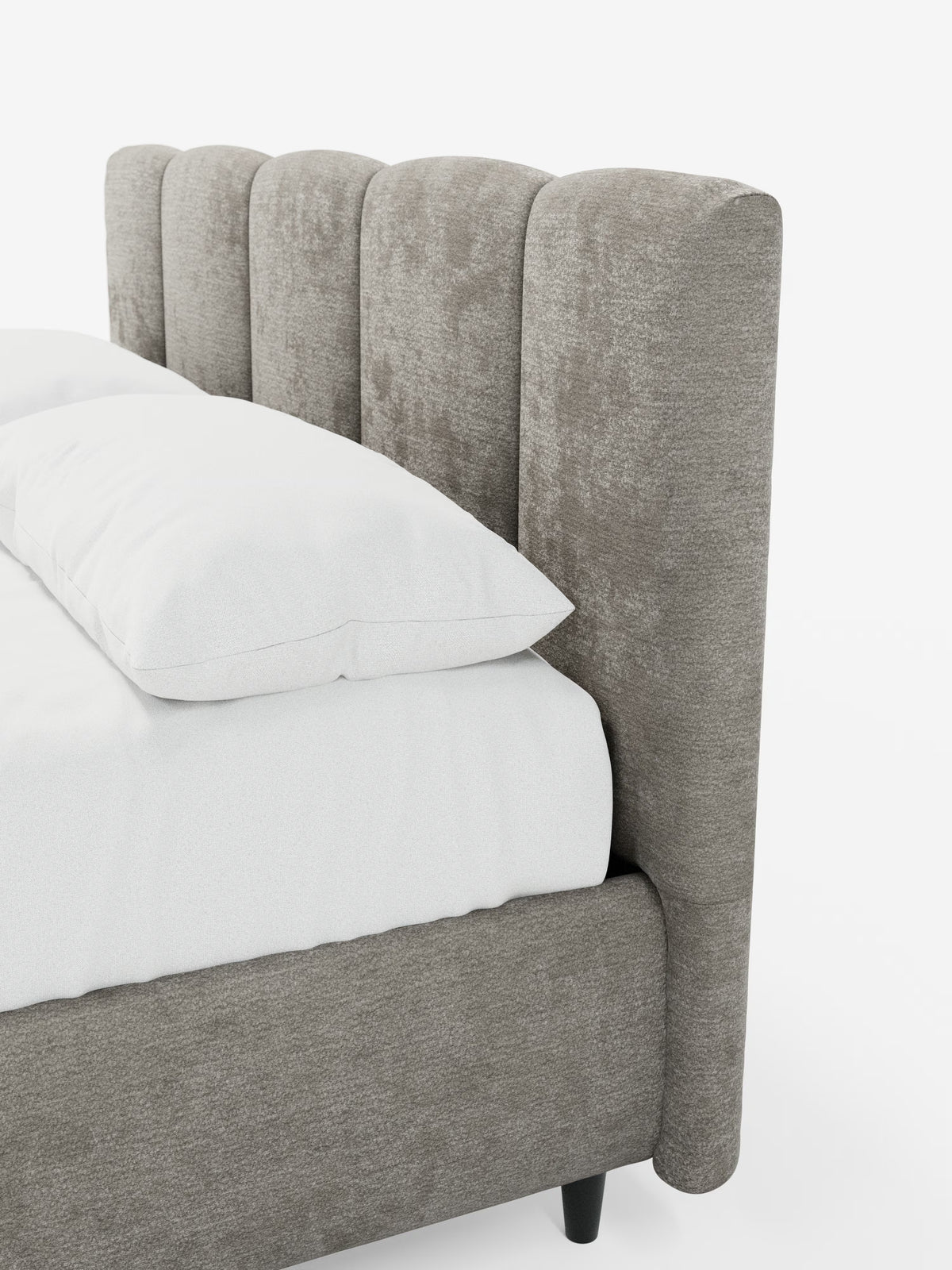 Un primo piano del letto imbottito ARKAM con contenitore e testiera a lavorazione verticale di Letti.store, caratterizzato da una testiera alta, con scanalature verticali, di colore grigio chiaro, imbottita in tessuto certificato Oeko-Tex®. Il materasso è rivestito con biancheria da letto e cuscini bianchi. Questo letto in stile shabby chic comprende una struttura imbottita abbinata con gambe corte e scure. Il tutto su uno sfondo bianco a tinta unita.