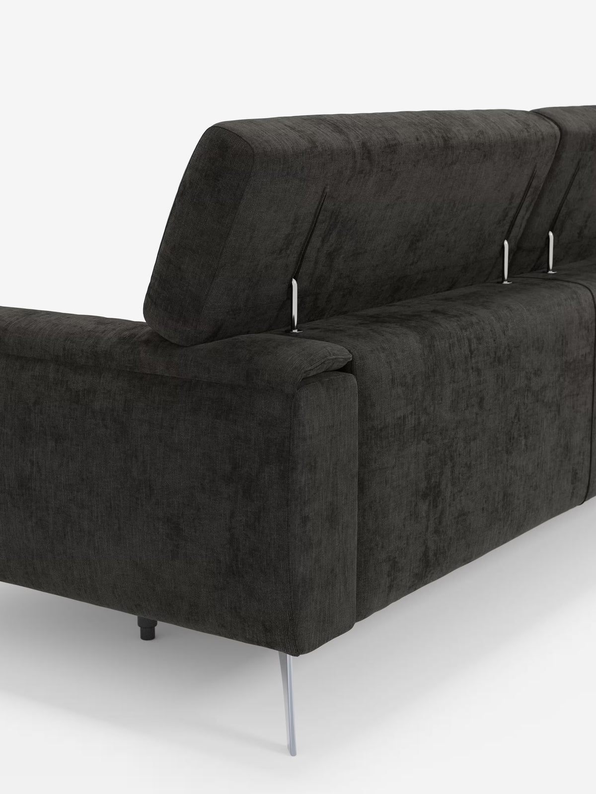 Un primo piano del divano Caravaggio a 2 e 3 posti con sedute allungabili e poggiatesta reclinabili, rivestito in elegante tessuto smacchiabile T31 di Divani.Store, ripreso dal retro in tessuto grigio scuro con effetto testurizzato. I poggiatesta regolabili sono sostenuti da sottili aste metalliche argentate, mentre sotto sono visibili le gambe slanciate anch'esse argentate. Lo sfondo è bianco a tinta unita.