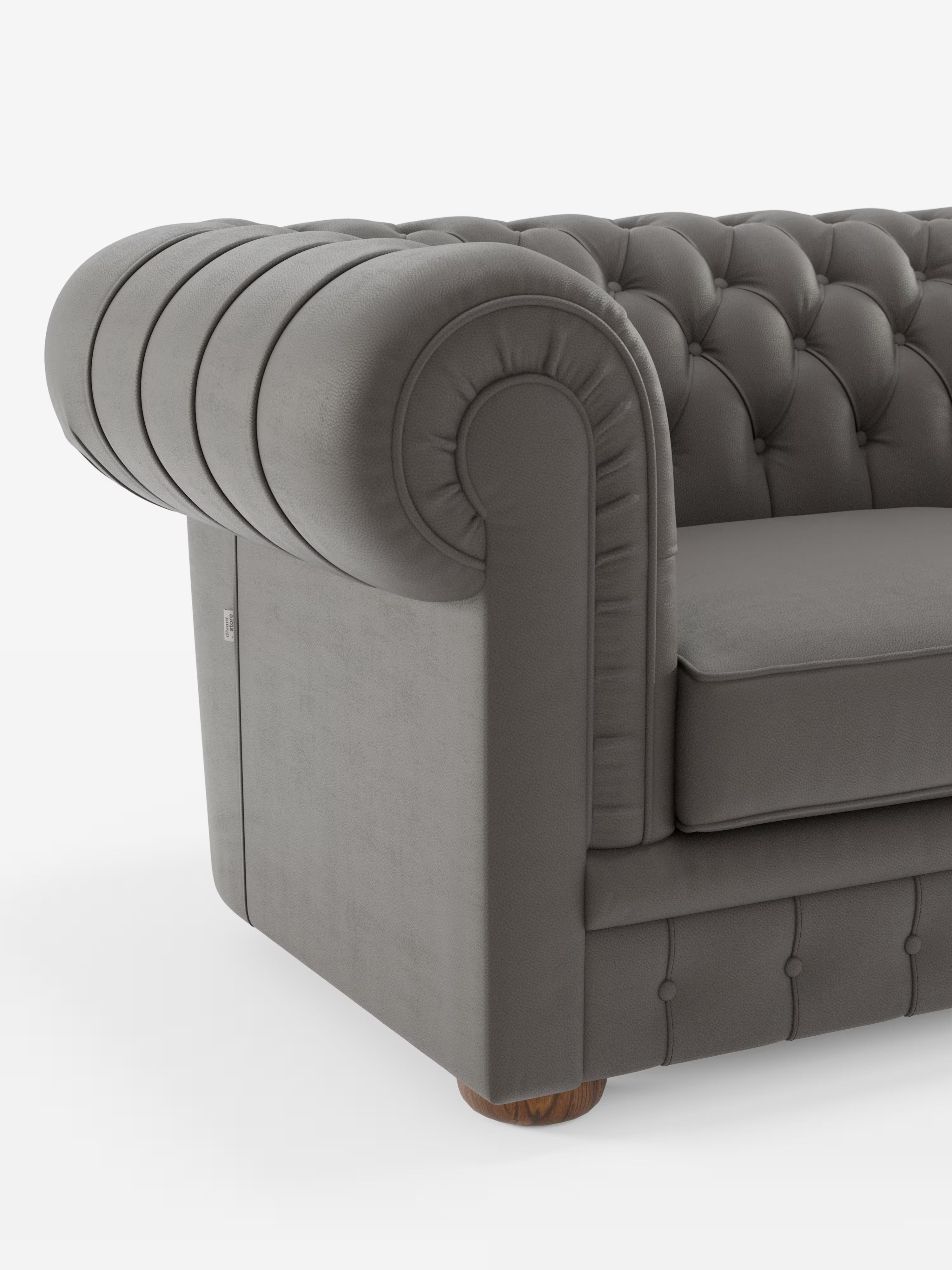 Primo piano di un Chester grigio – Divano Chesterfield in vera pelle spessorata a 2 e 3 posti di Divani.Store, caratterizzato da braccioli arrotondati, trapuntatura a bottoni e morbidi cuscini di seduta. Questo divano artigianale italiano poggia su gambe corte e rotonde in legno, in primo piano su uno sfondo bianco a tinta unita. Sono visibili solo il bracciolo sinistro e una parte della seduta.
