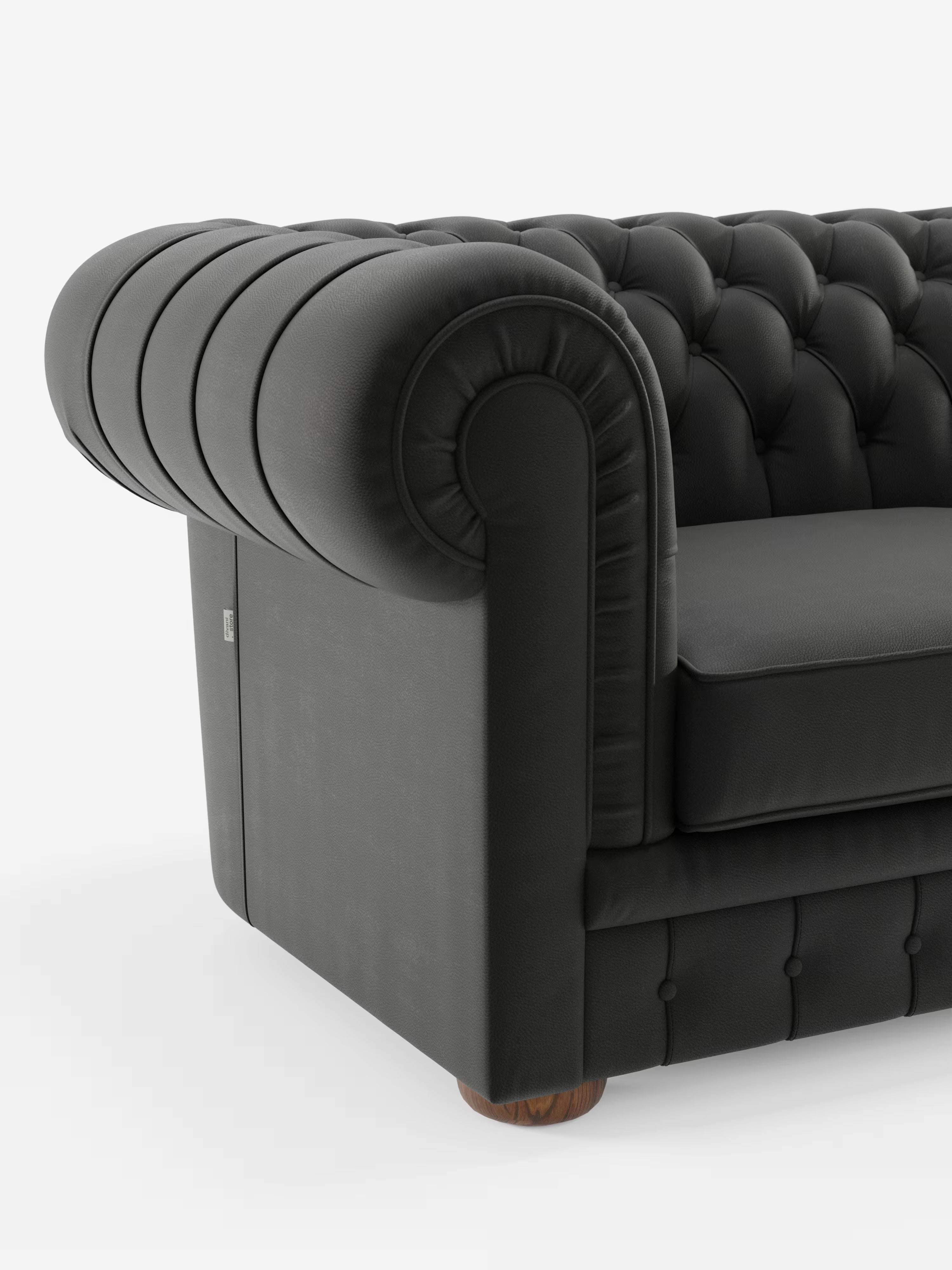 Primo piano del bracciolo sinistro di Chester, un divano Chesterfield grigio scuro con imbottitura a ciuffetti, realizzato in vera pelle spessa da Divani.Store, caratterizzato da braccioli arrotondati, profondi bottoni decorativi e piedini arrotondati in legno, su uno sfondo bianco a tinta unita. Questo elegante divano artigianale è orgogliosamente prodotto in Italia.